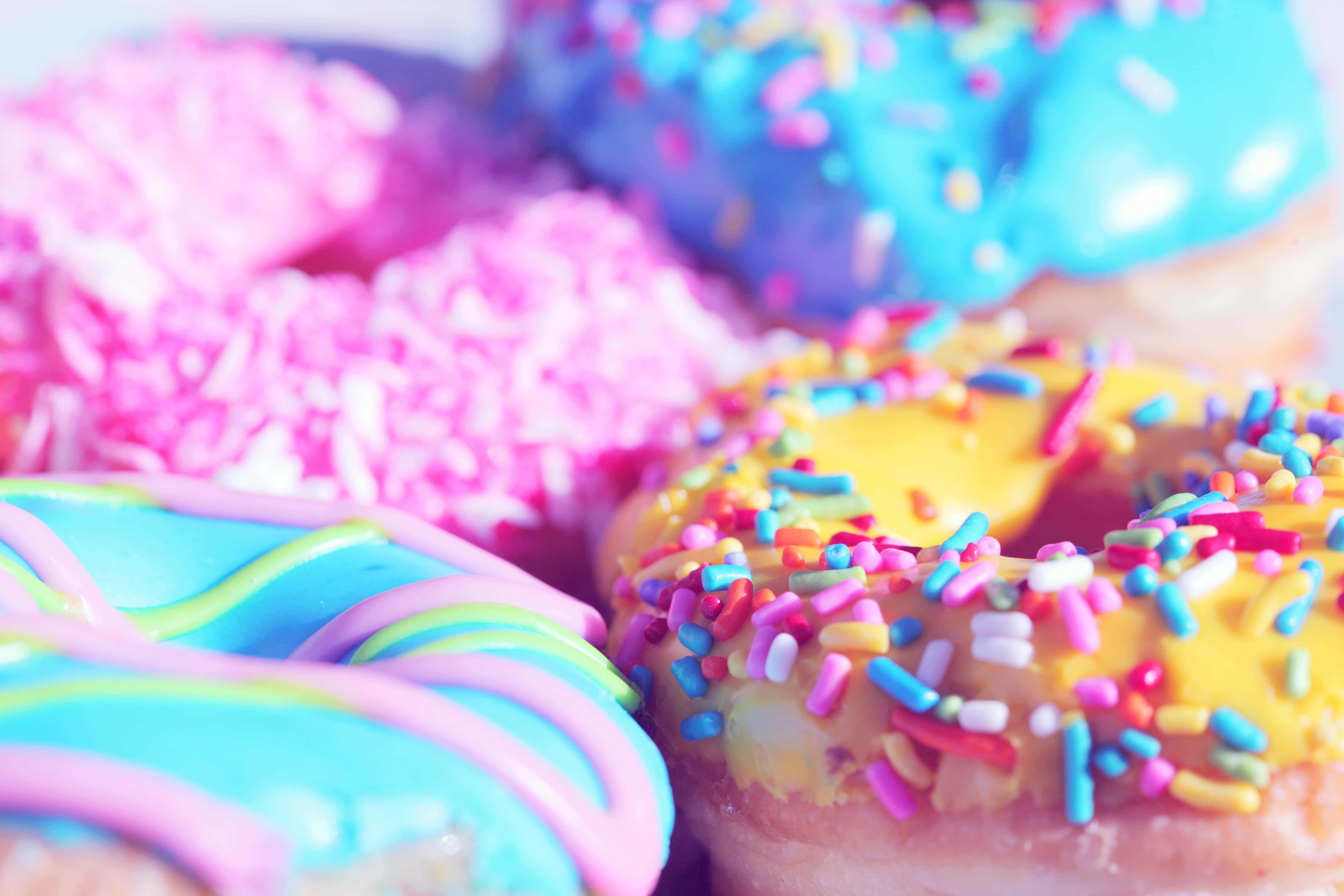 Cute Donut 桌布 壁紙 — 色彩繽紛的甜甜圈特寫，帶有鮮豔的糖霜和彩虹糖針，營造出甜美的節日美食。