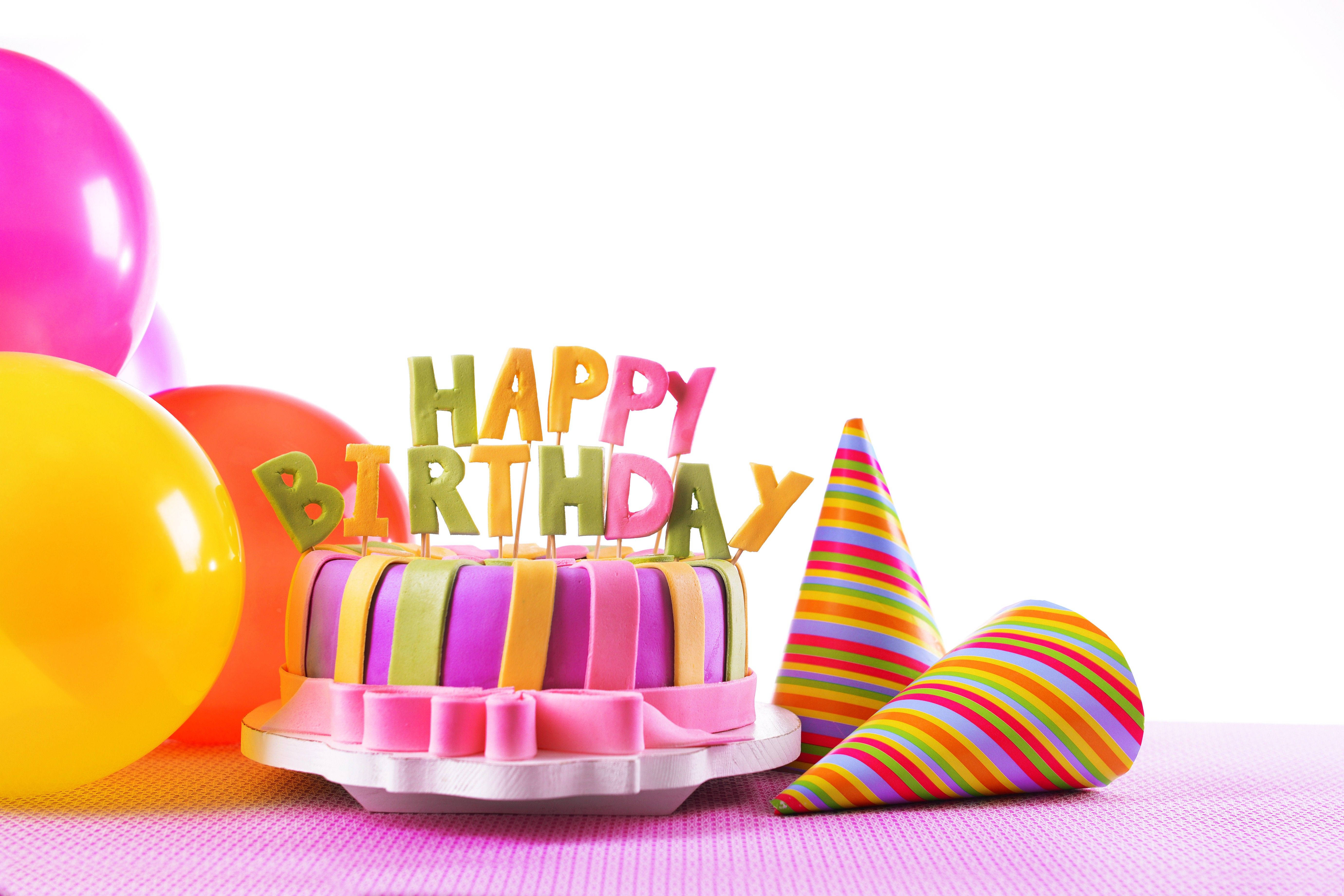 生日快樂 桌布 壁紙 — 色彩繽紛的生日蛋糕，帶有彩虹條紋糖霜和「生日快樂」字樣，周圍環繞著氣球和派對帽。