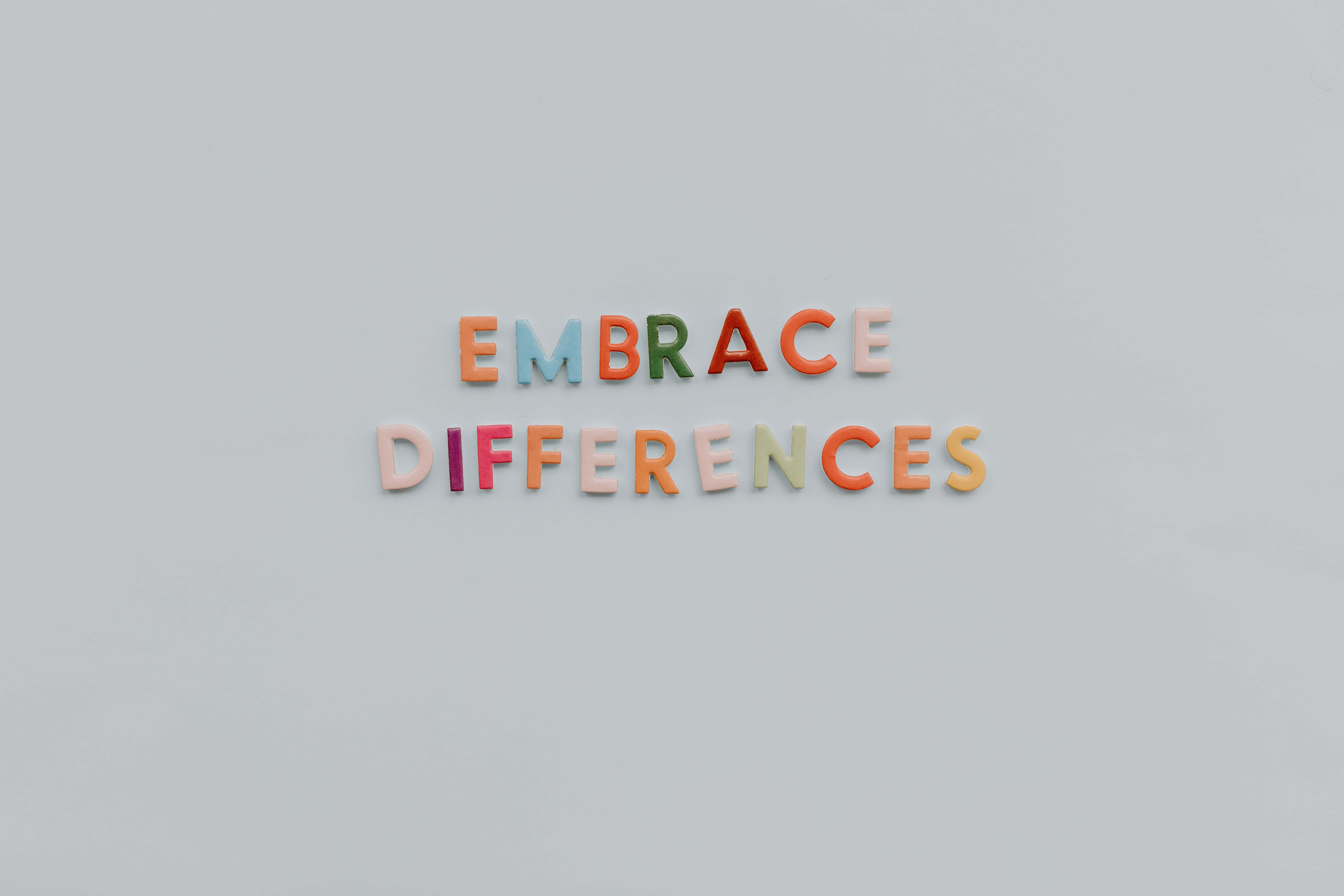 Autism 桌布 壁紙 — 色彩繽紛的磁鐵字母在純灰色表面上拼出「EMBRACE DIFFERENCES」。