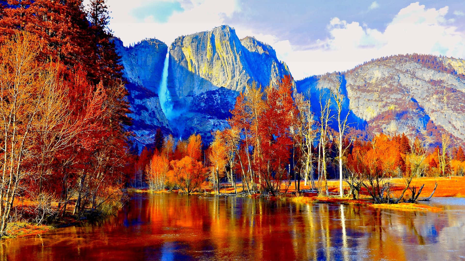 Fall Mountains 桌布 壁紙 — 色彩繽紛的秋樹在平靜的水面上倒映，前方是高聳的山脈和層疊的瀑布，天空部分多雲。