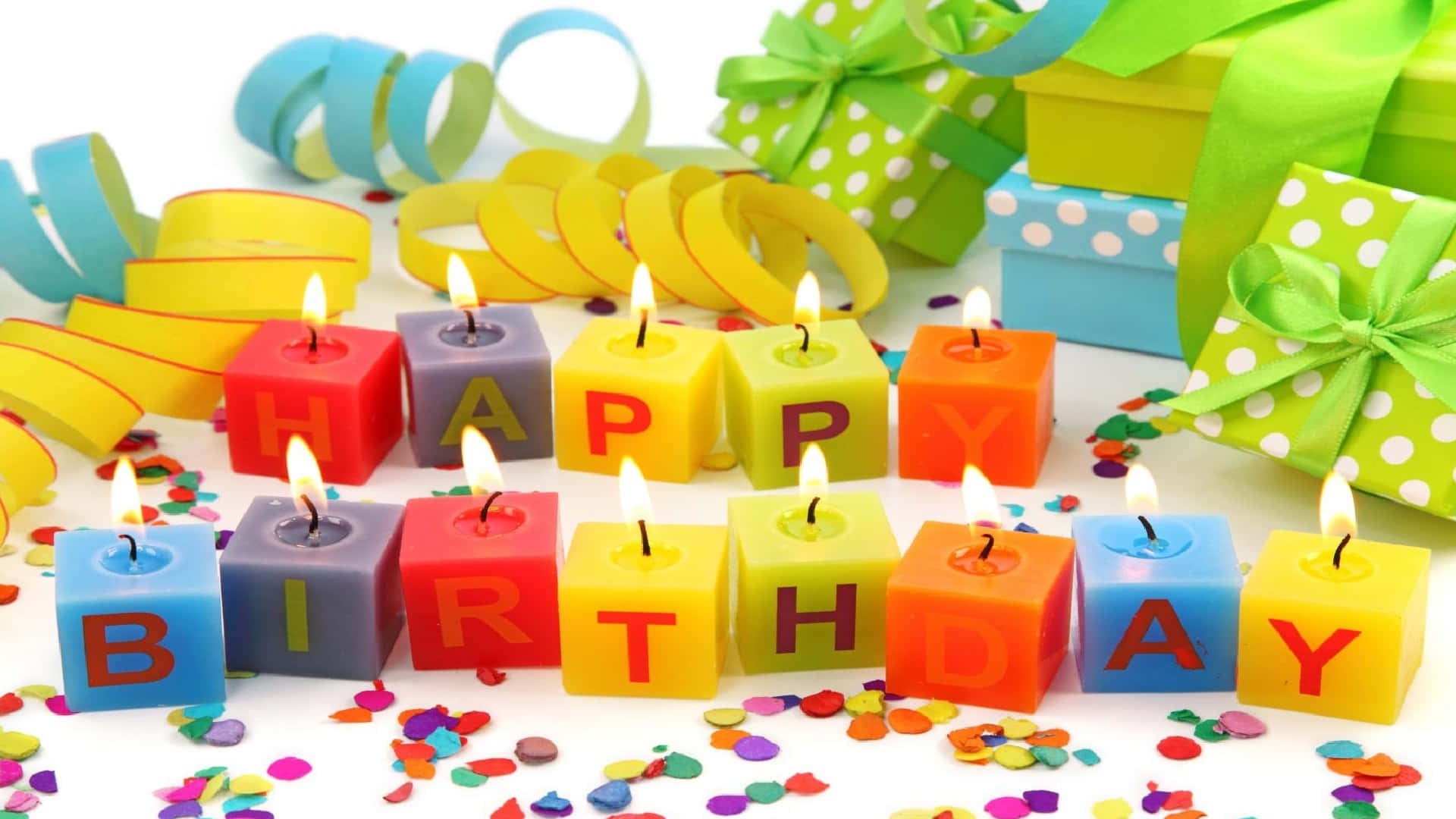 High Resolution Happy Birthday 桌布 壁紙 — 色彩繽紛的立方體蠟燭拼出 happy birthday，在五彩紙屑和包裝好的禮物中溫暖地發光。