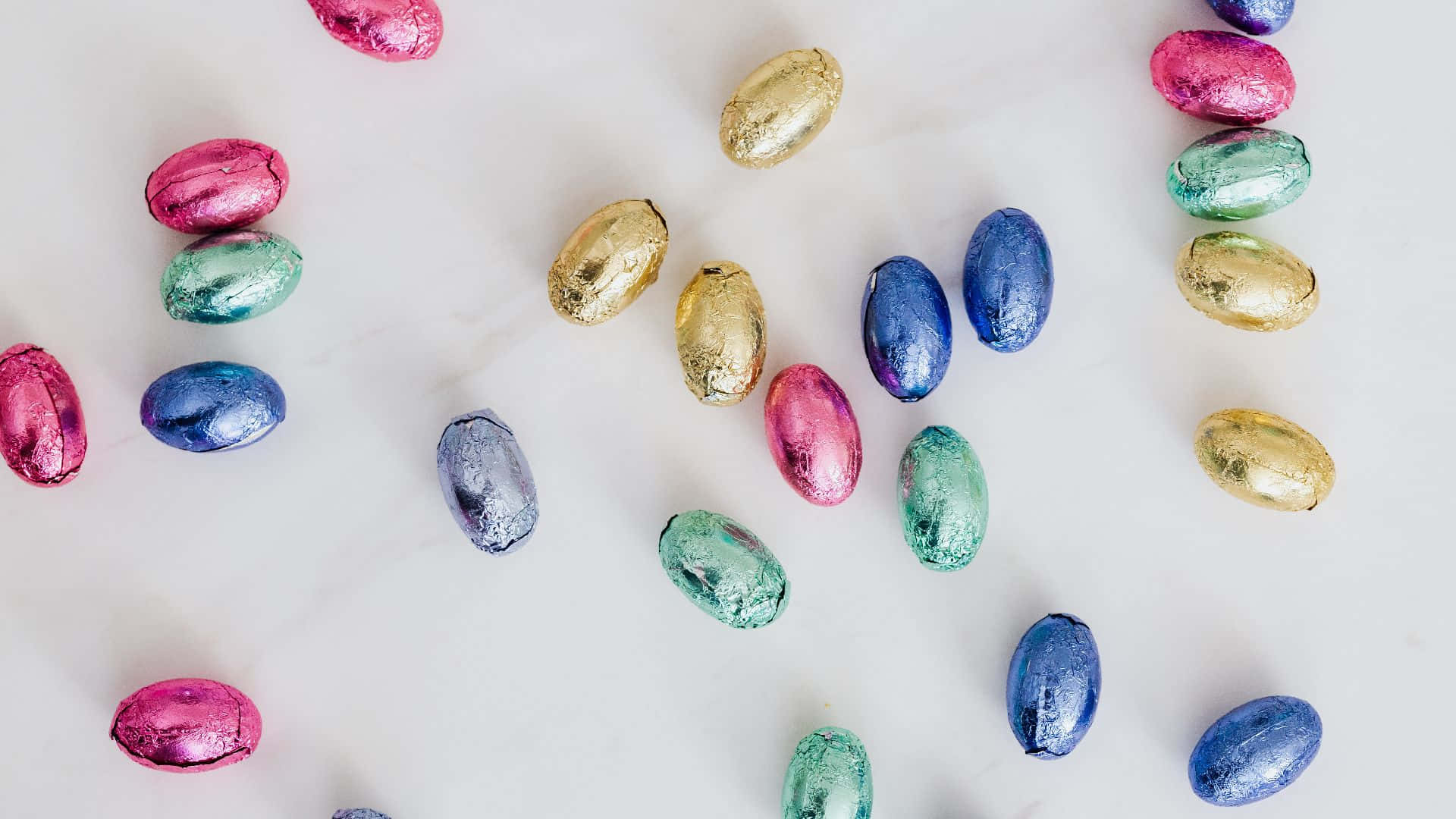 Easter Zoom 桌布 壁紙 — 色彩繽紛的箔紙包裹巧克力蛋散落在白色大理石表面上，形成節日圖案。