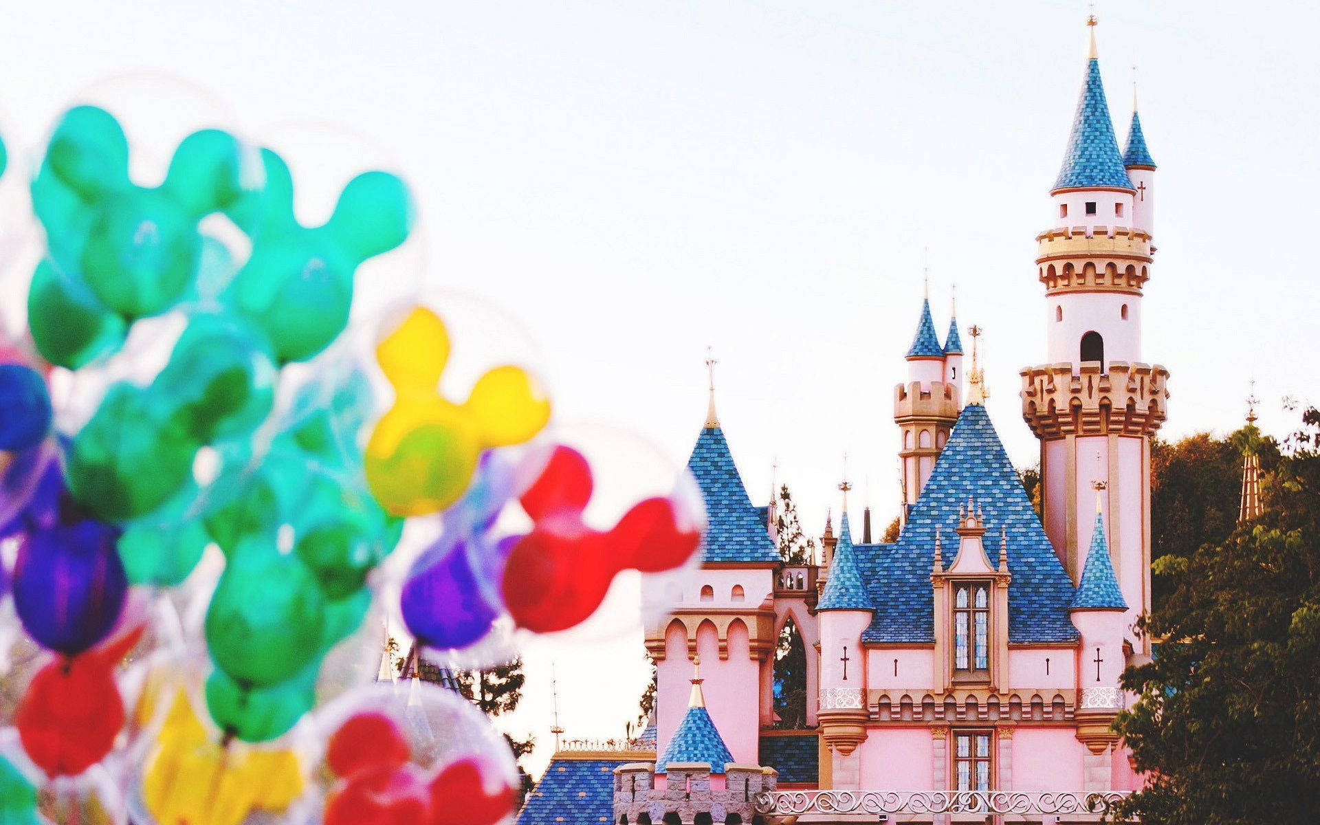 Disneyland Castle 桌布 壁紙 — 色彩繽紛的米奇老鼠氣球在前景飄浮，背景是柔焦的睡美人城堡。