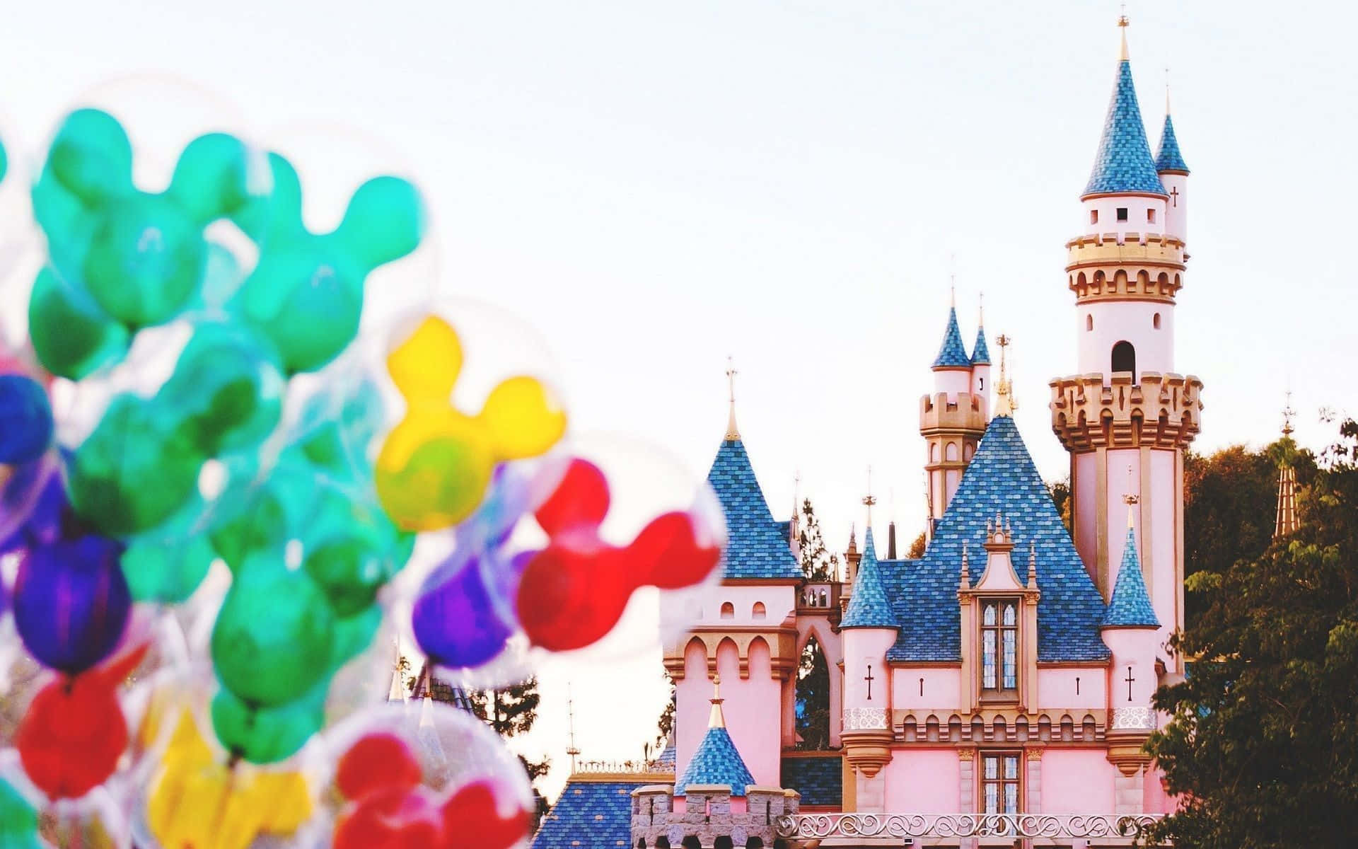 Disney Castle 桌布 壁紙 — 色彩繽紛的米奇老鼠氣球在前景飄浮，背景是柔焦的睡美人城堡。