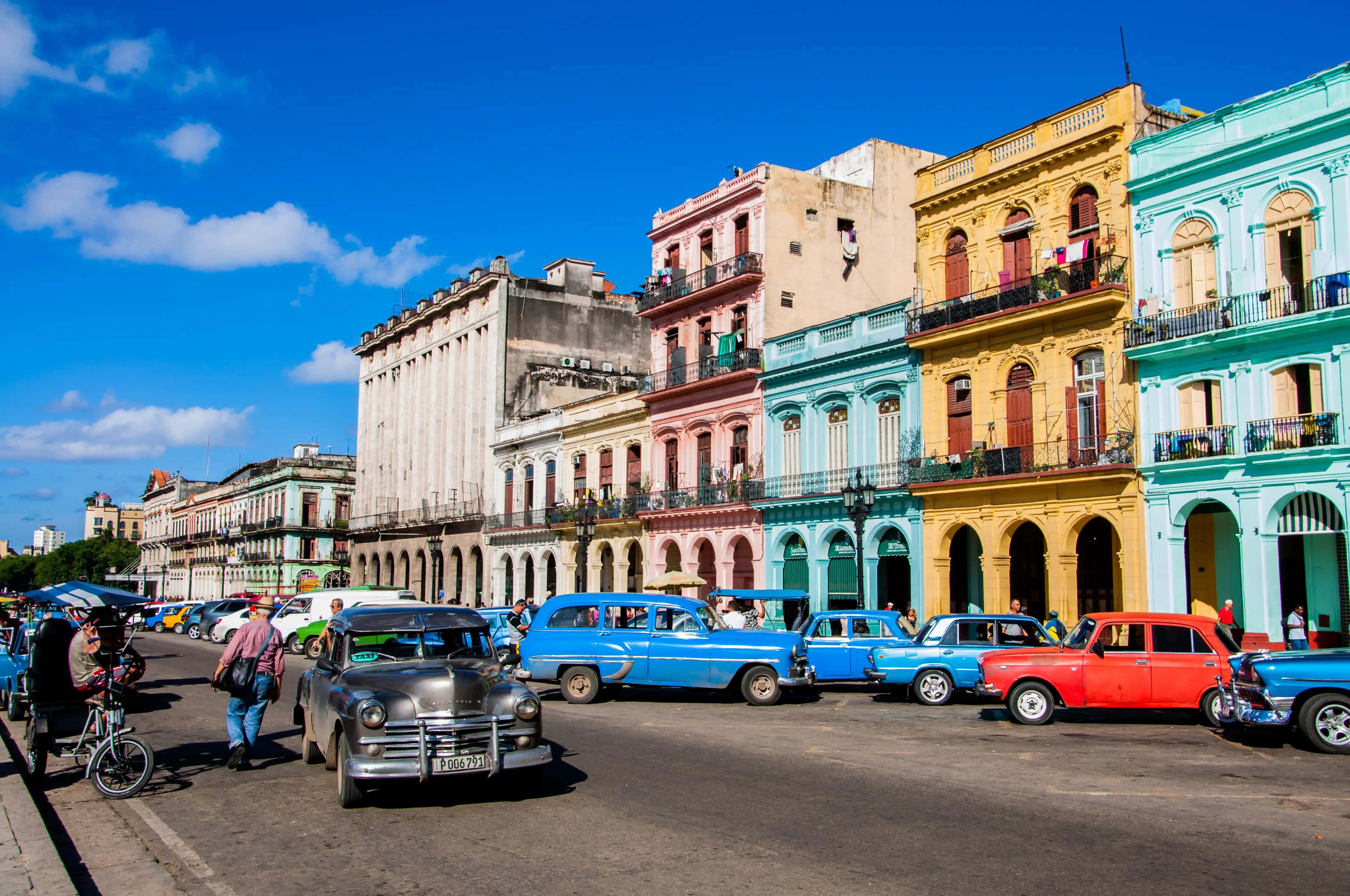 Cuba 桌布 壁紙 — 色彩繽紛的粉彩色殖民建築排列在繁忙的街道上，街道上充滿經典復古汽車，天空湛藍明亮。