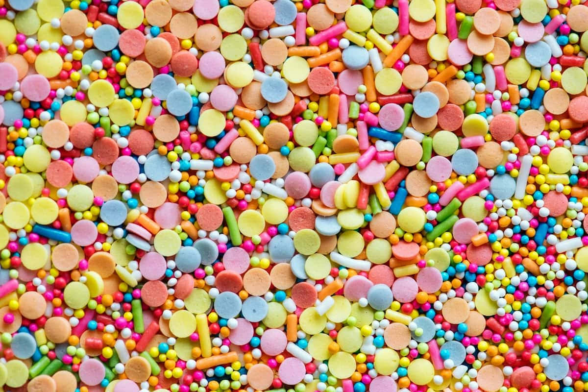 糖果 桌布 壁紙 — 色彩繽紛的糖果碎屑特寫，有圓形、條狀和球狀，營造出甜蜜的節日質感。
