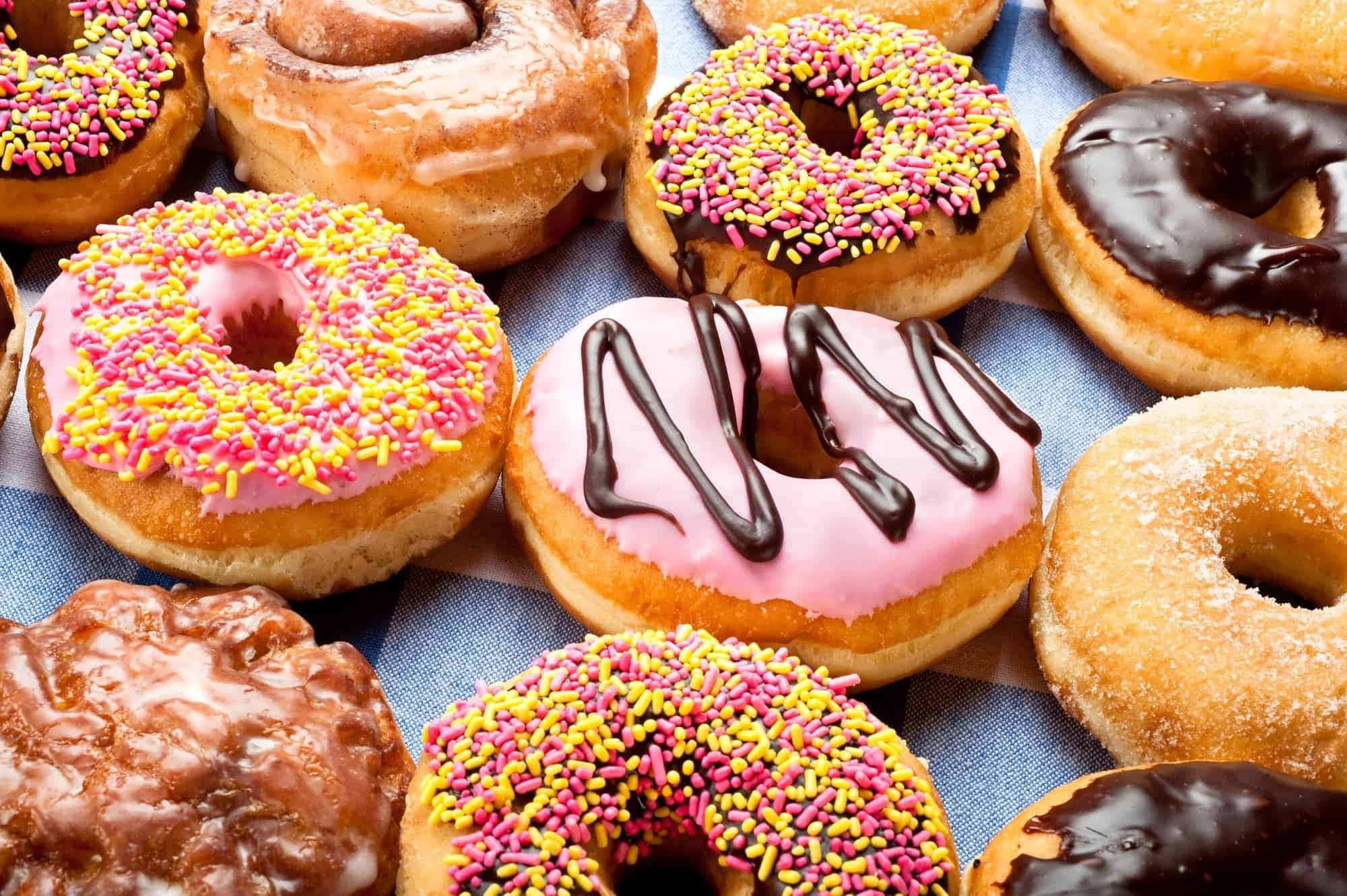 Dunkin Donuts 桌布 壁紙 — 色彩繽紛的糖霜和彩針甜甜圈排列在藍色格紋布上。