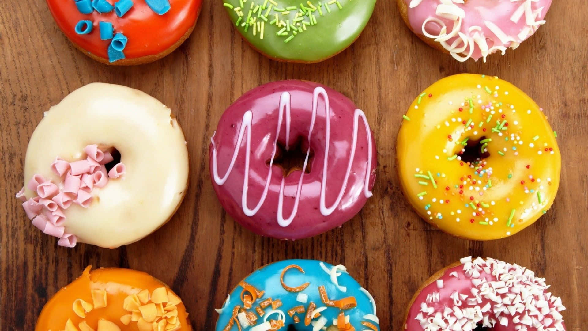 donuts 桌布 壁紙 — 色彩繽紛的糖霜甜甜圈，上面灑滿彩色糖針，整齊排列在溫暖的木質表面上。