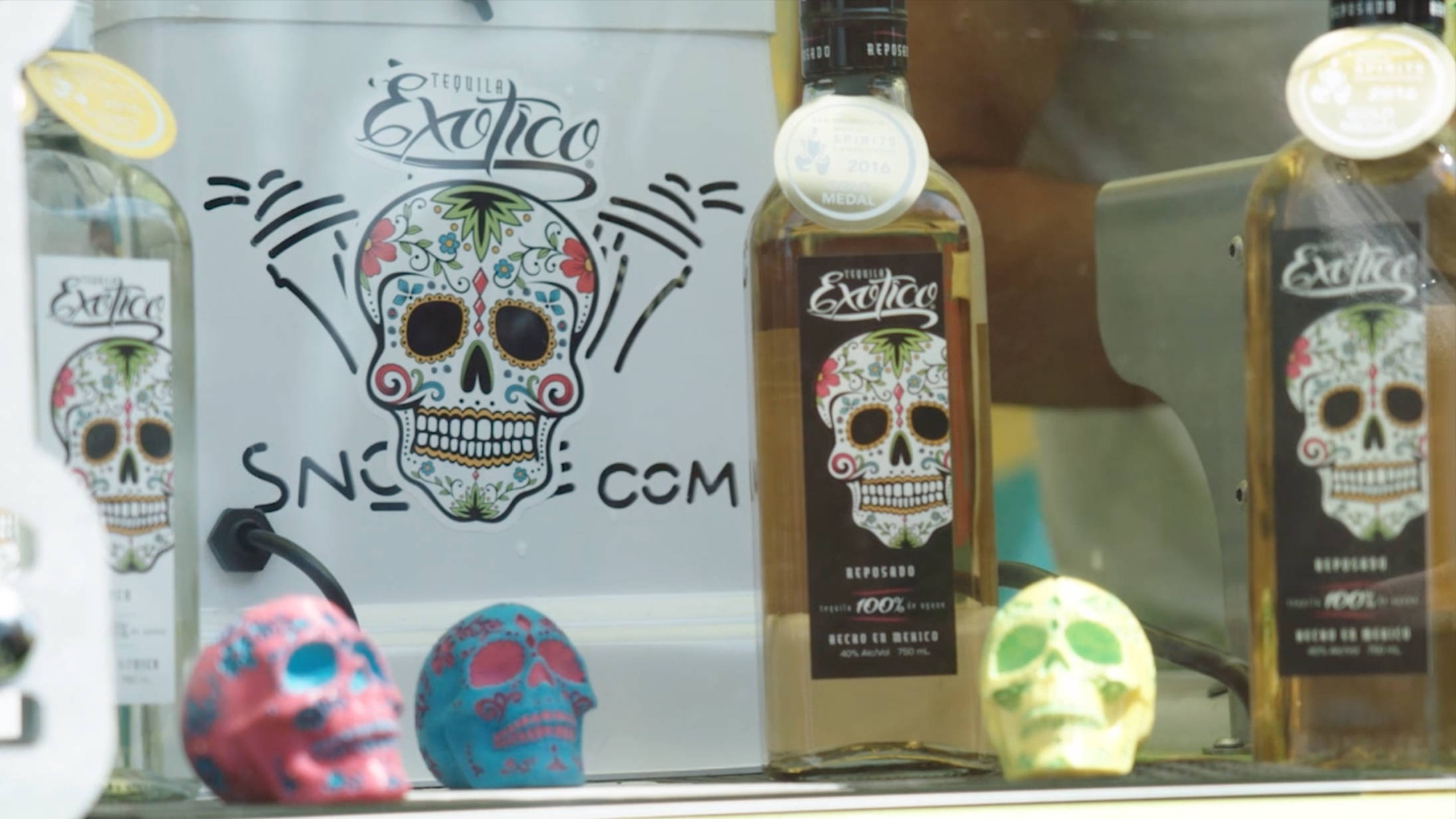 bottle 桌布 壁紙 — 色彩繽紛的糖骷髏裝飾和Exotico龍舌蘭酒瓶展示在玻璃陳列櫃中，並帶有品牌標誌。