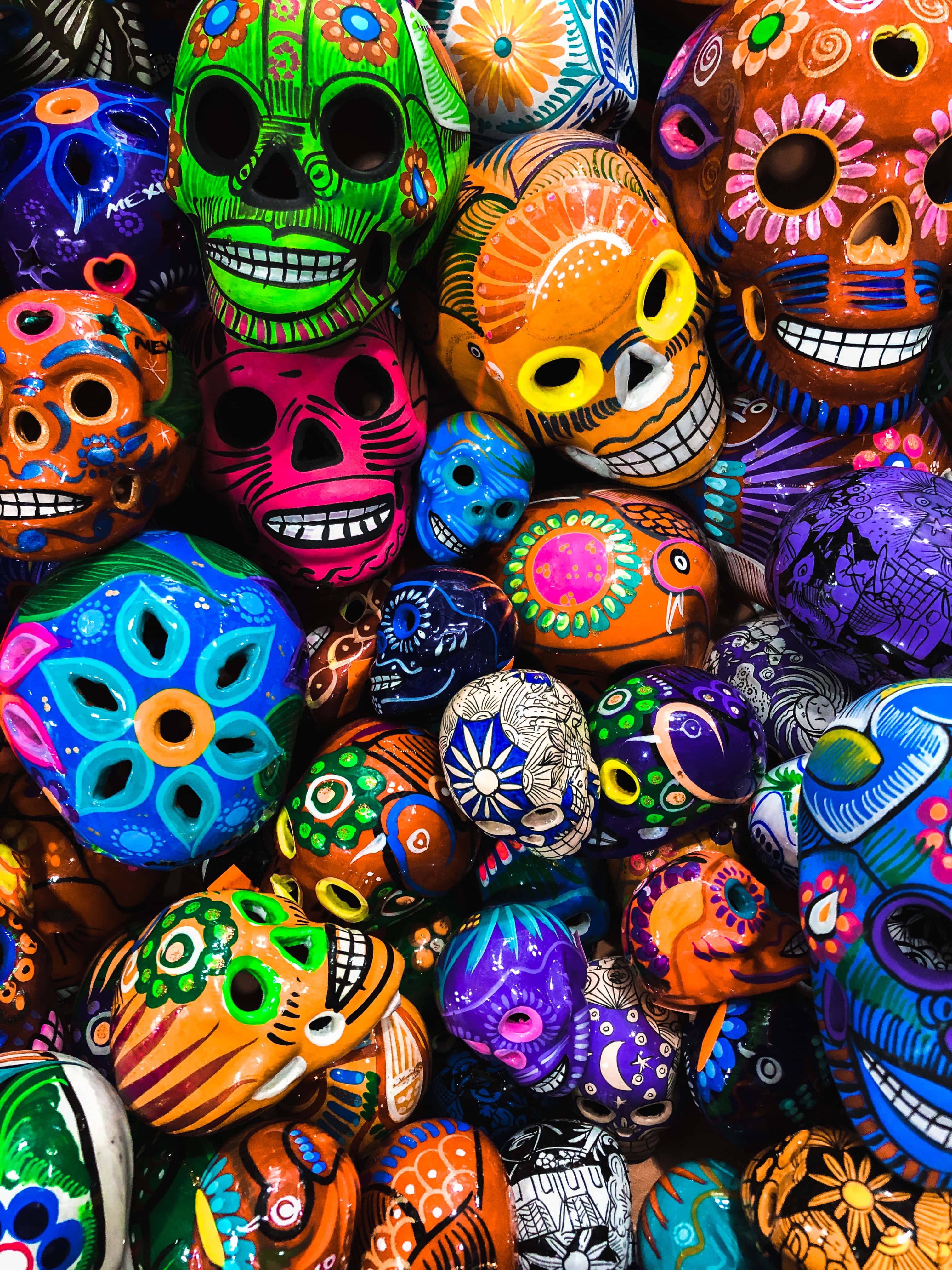 Mexican 桌布 壁紙 — 色彩繽紛的糖骷髏頭，帶有複雜的花卉圖案和明亮的色調，堆疊在一起形成節日展示。