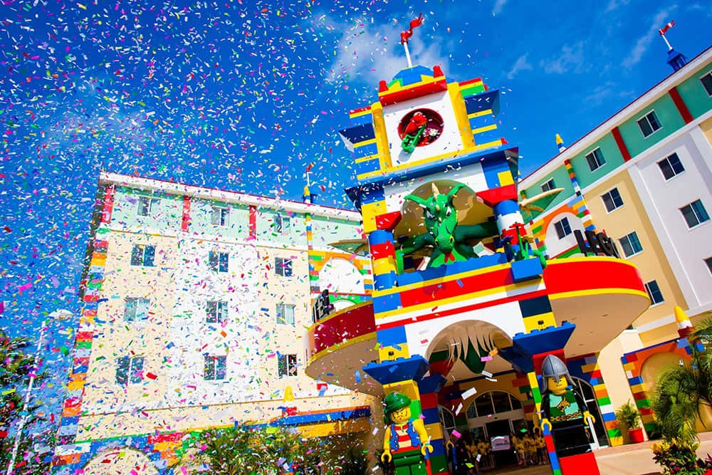 Legoland 桌布 壁紙 — 色彩繽紛的紙屑灑落在一個充滿活力的LEGO主題建築上，建築物有龍雕像和迷你人偶，背景是明亮的藍天。