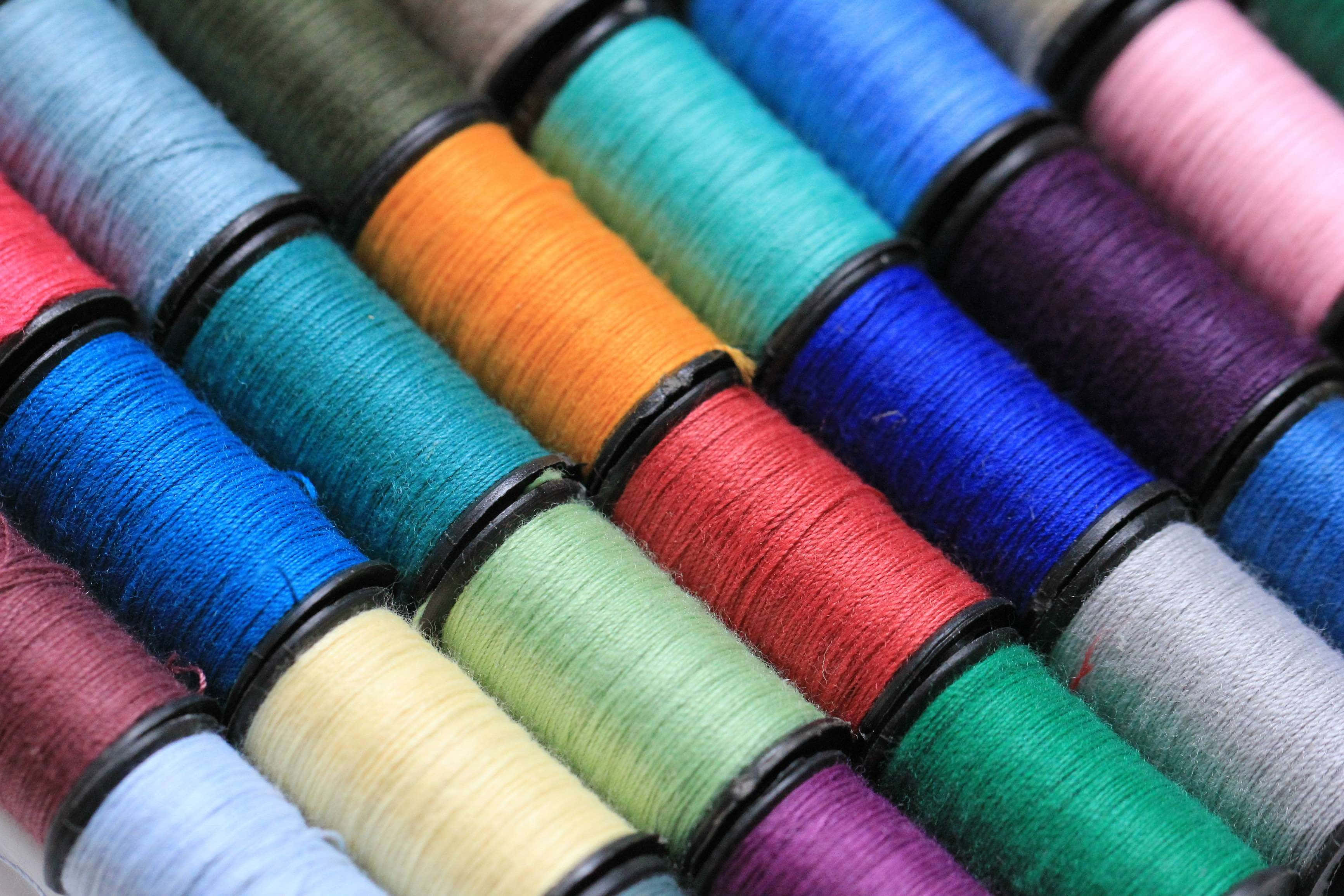 clothing 桌布 壁紙 — 色彩繽紛的線軸以彩虹色調對角排列的特寫，可見紋理纖維。
