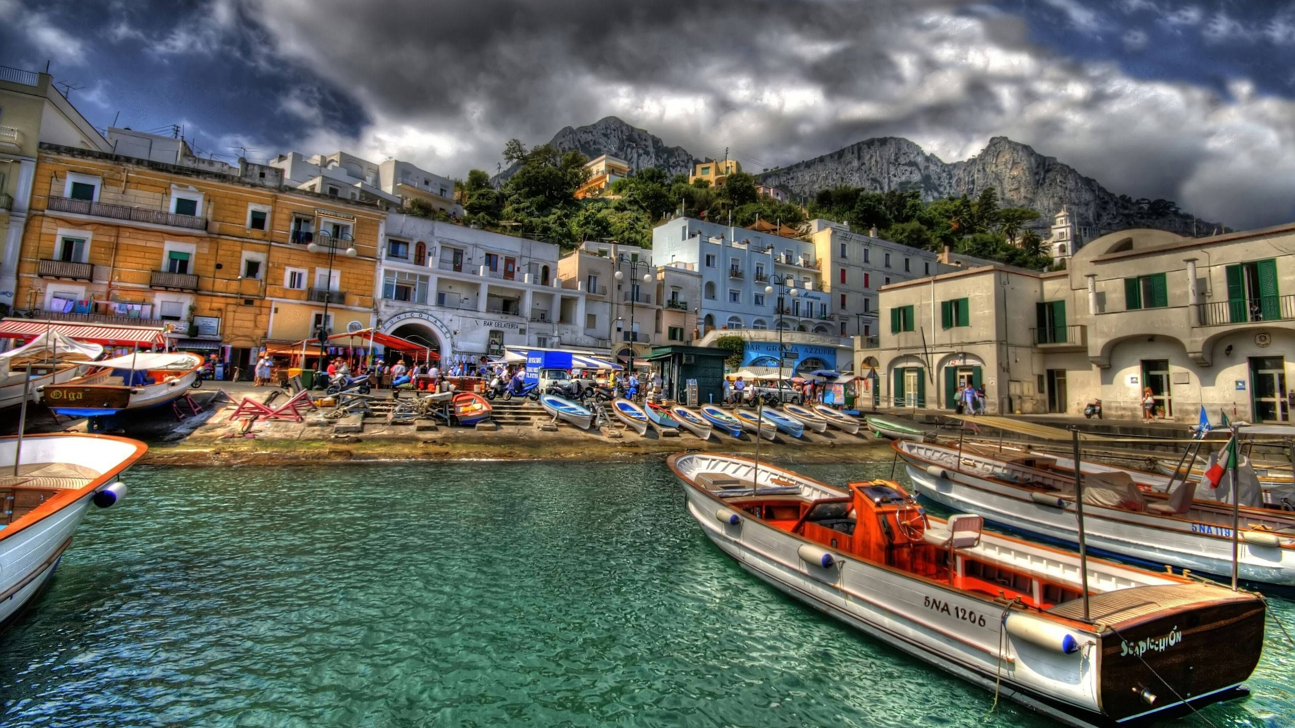 Capri 桌布 壁紙 — 色彩繽紛的船隻在熱鬧的地中海港口的碧綠海水中停泊，上方是戲劇性的暴風雲。
