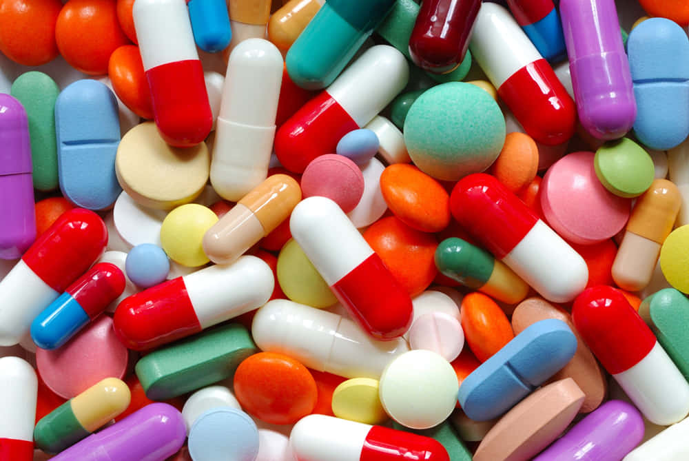 pills 桌布 壁紙 — 色彩繽紛的藥丸和膠囊密集散落，形成混亂但視覺上引人注目的堆疊特寫。