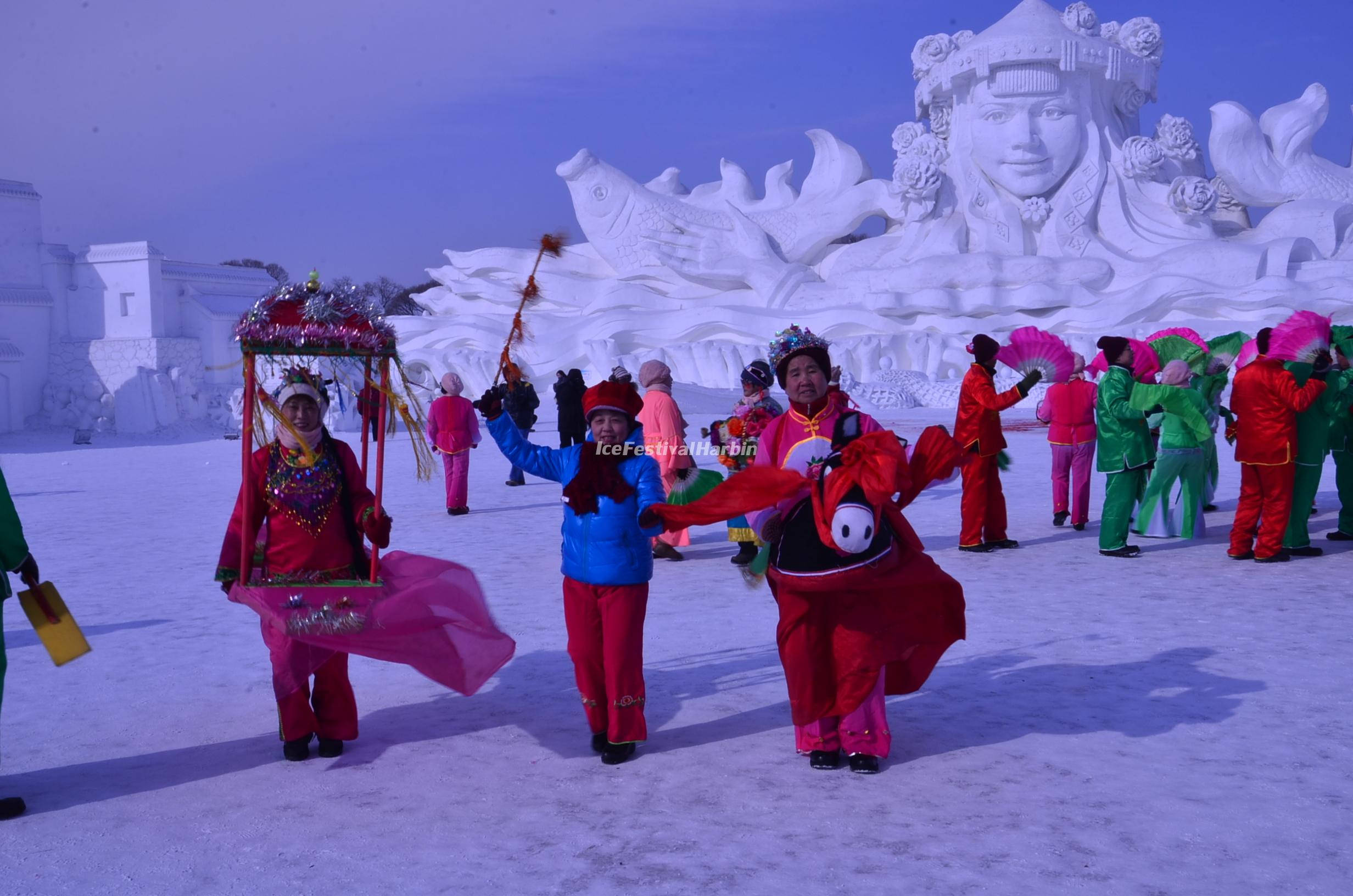 Harbin 桌布 壁紙 — 色彩繽紛的表演者在雪地上歡快地跳舞，背景是一座巨大而精緻的雪雕。