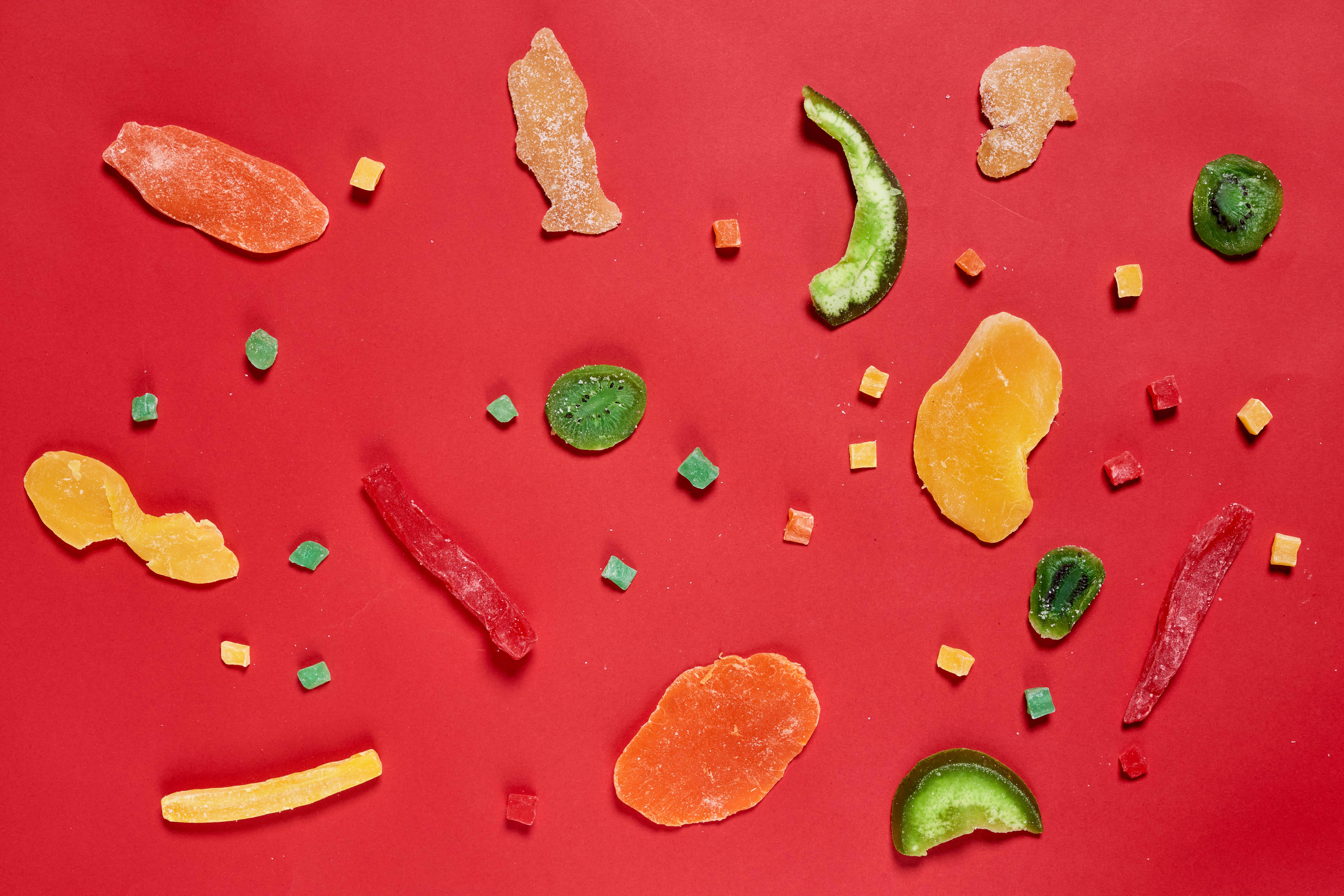 Fruits 桌布 壁紙 — 色彩繽紛的軟糖以各種形狀和顏色散落在鮮明的紅色背景上。