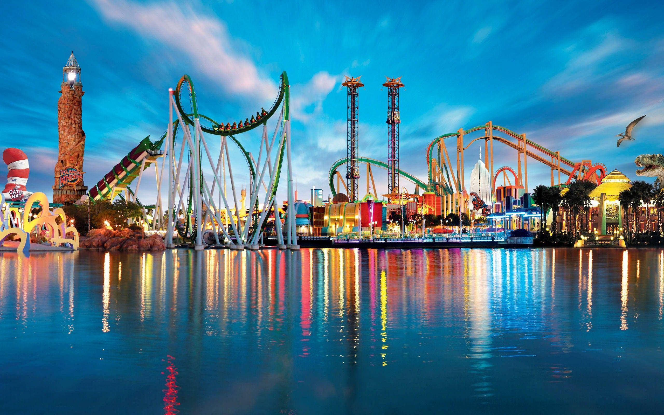 Theme Park 桌布 壁紙 — 色彩繽紛的遊樂園遊樂設施在暮色天空下發光，倒映在平靜的水面上。
