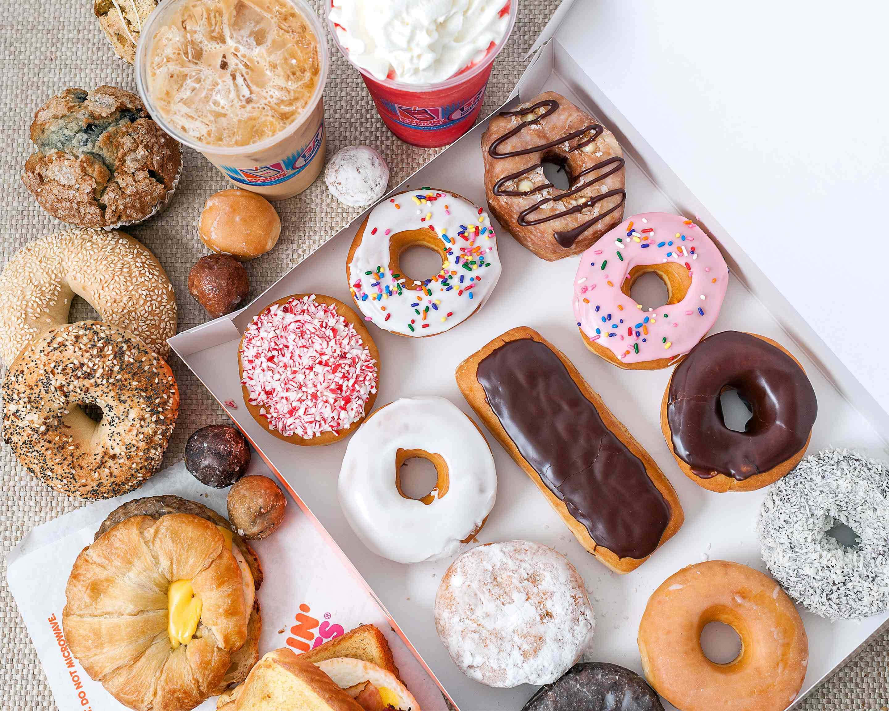 Dunkin Donuts 桌布 壁紙 — 色彩繽紛的釉面灑巧克力粉和糖粉甜甜圈、貝果和糕點，排列在紋理表面上，搭配冰咖啡和鮮奶油。