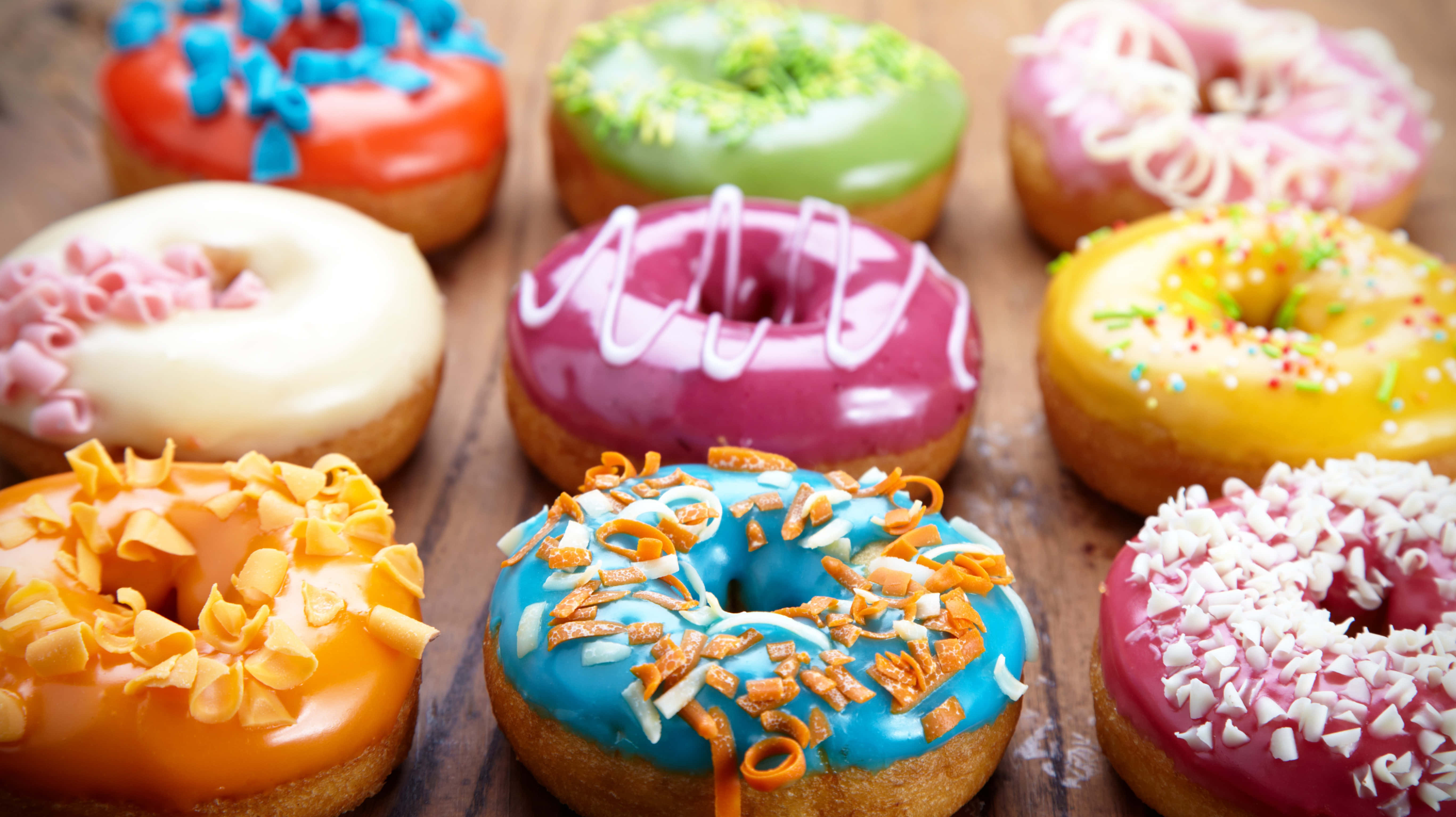 Donut 桌布 壁紙 — 色彩繽紛的釉面甜甜圈，搭配彩色配料，擺放在質樸的木質表面上。
