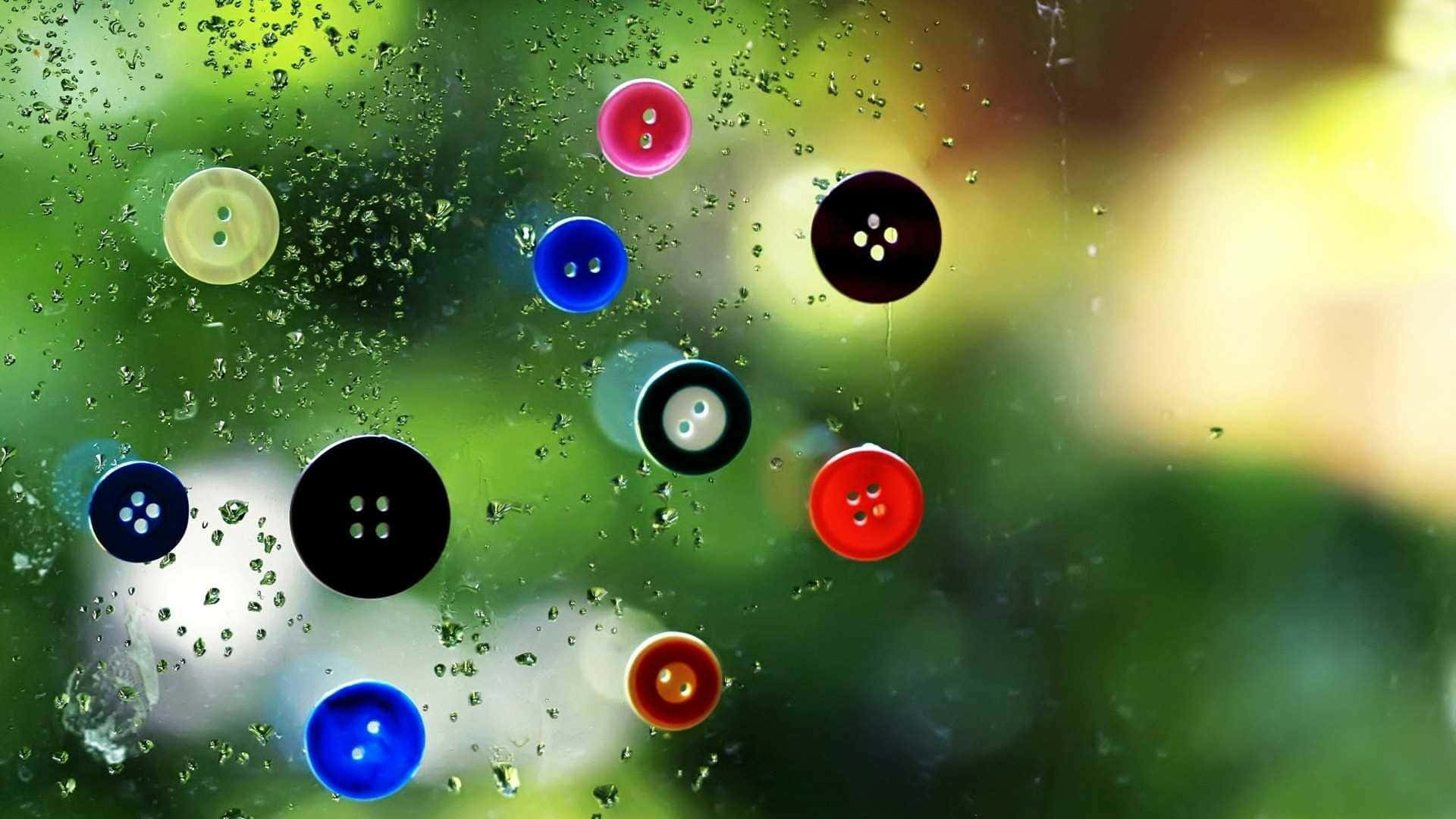 桌布 壁紙 — 色彩繽紛的鈕扣緊貼在沾滿雨點的窗戶上，窗外是模糊的綠色樹葉。