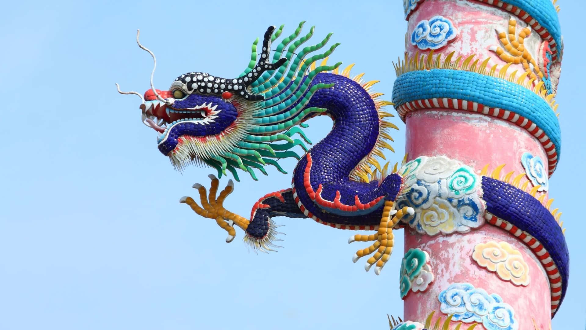 Blue Dragon 桌布 壁紙 — 色彩繽紛的陶瓷龍雕塑纏繞在彩色柱子上，襯托著清澈的藍天。
