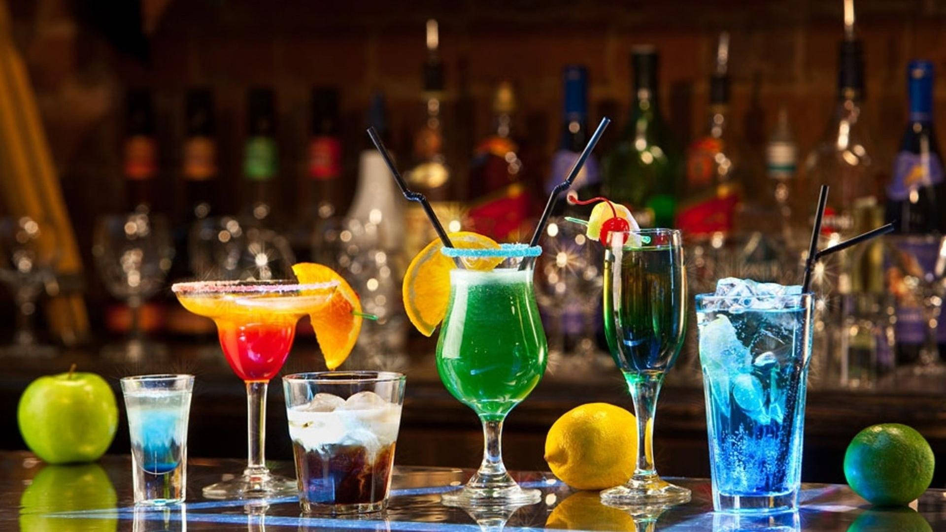 Drink 桌布 壁紙 — 色彩繽紛的雞尾酒在彩色玻璃杯中，配上水果裝飾，放在吧檯上，背景中的瓶子模糊不清。