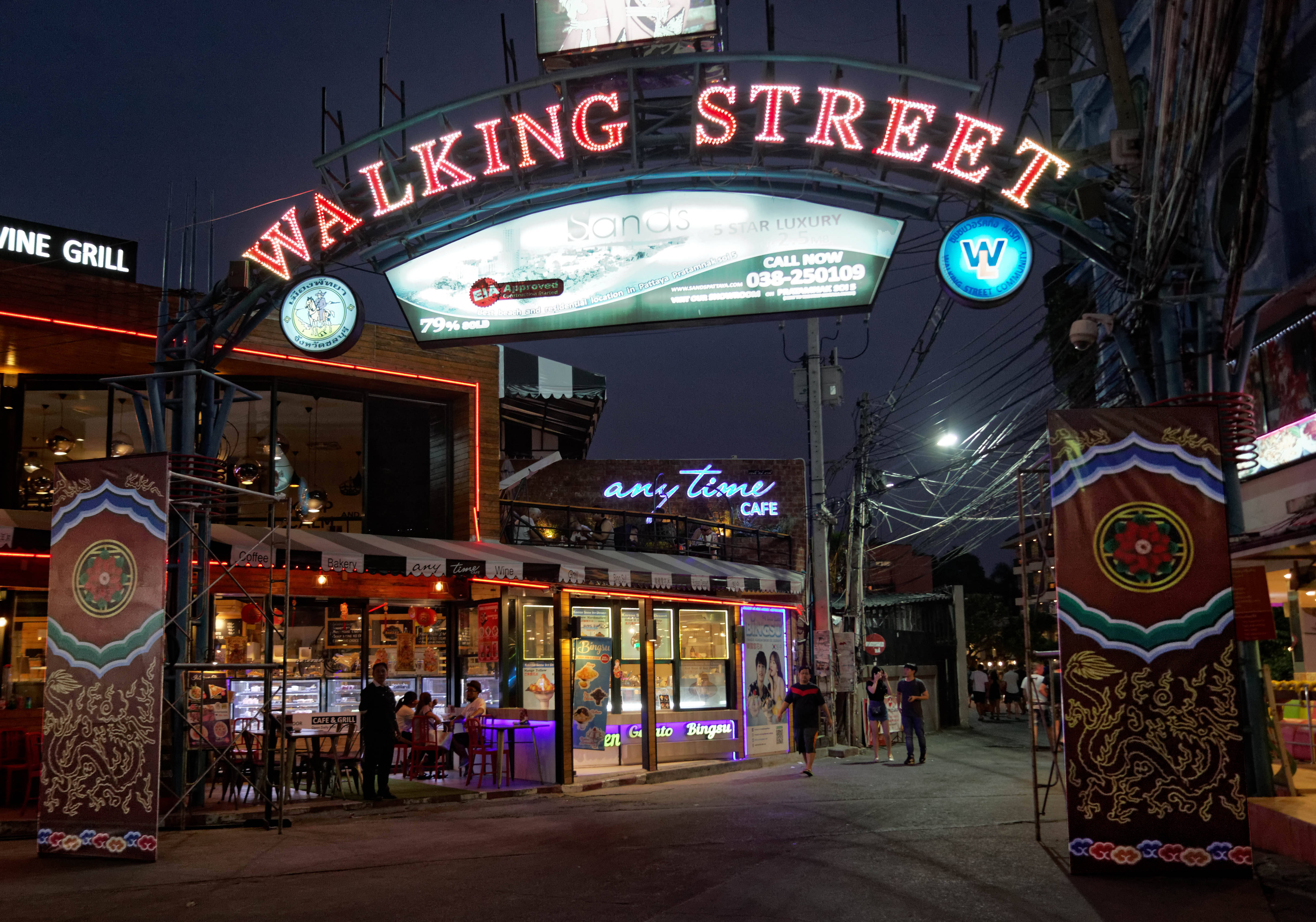 城市 桌布 壁紙 — 色彩繽紛的霓虹招牌寫著「WALKING STREET」，照亮了熱鬧的夜晚場景，人們在色彩繽紛的商店櫥窗和發光的咖啡館窗戶旁漫步。