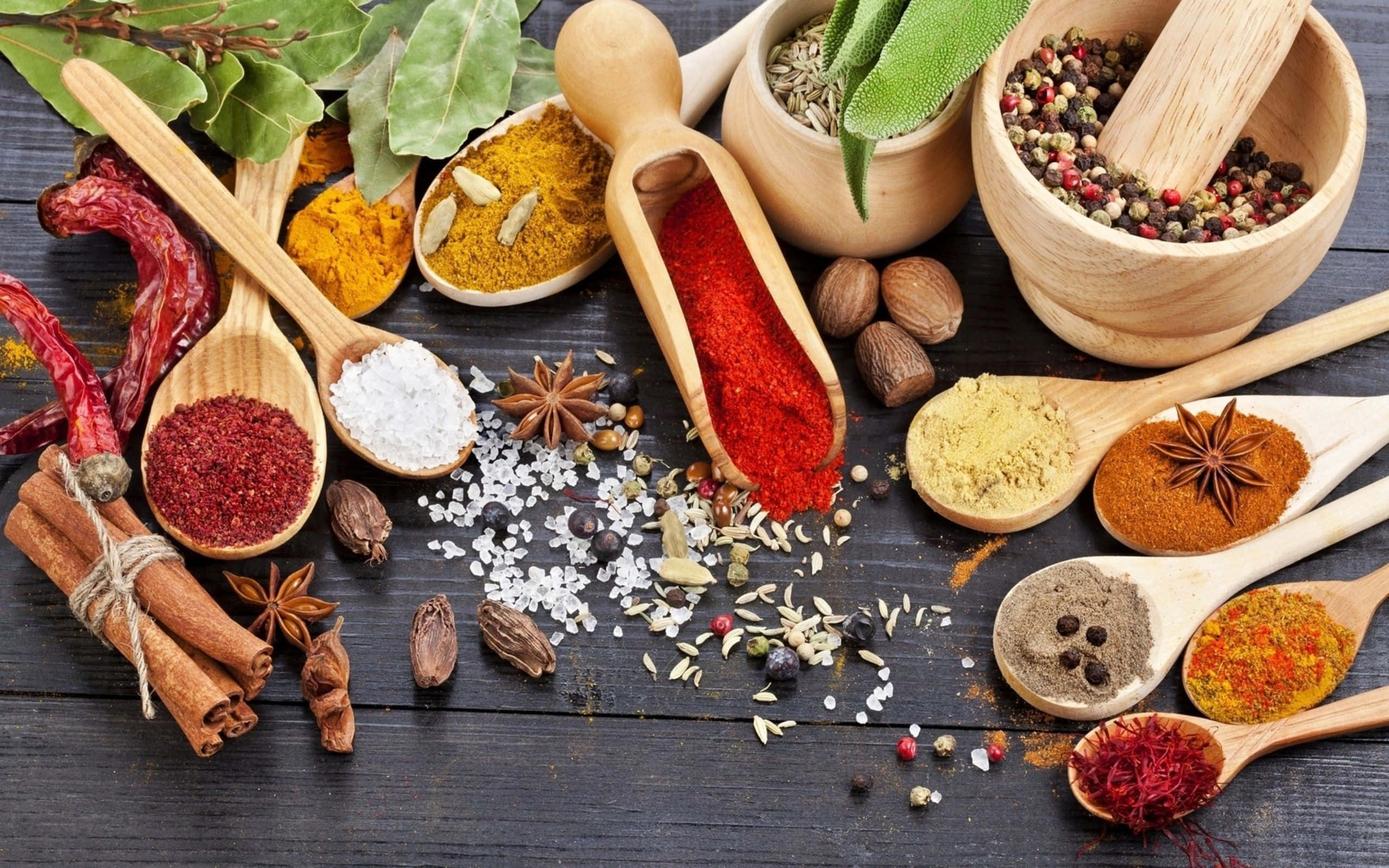 Spices 桌布 壁紙 — 色彩繽紛的香料和香草在木勺中，灑落在深色鄉村風木桌上。