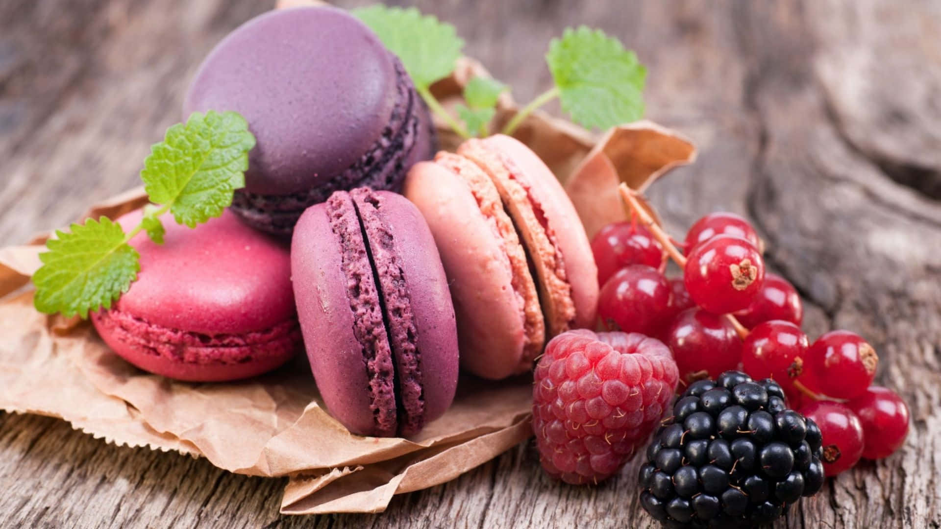 Desserts 桌布 壁紙 — 色彩繽紛的馬卡龍和新鮮莓果放在鄉村風木質表面上的皺紙上。