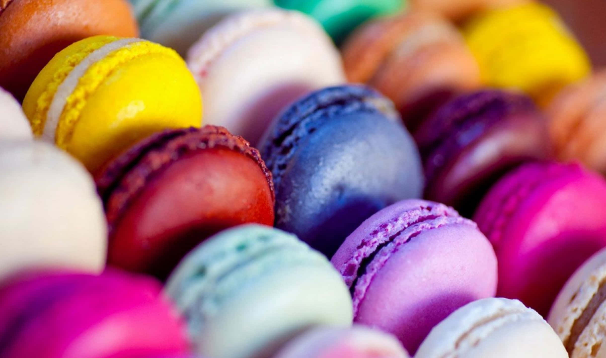 2440x1440 Desserts 桌布 壁紙 — 色彩繽紛的馬卡龍特寫，有光澤的外殼和精緻的褶邊邊緣。