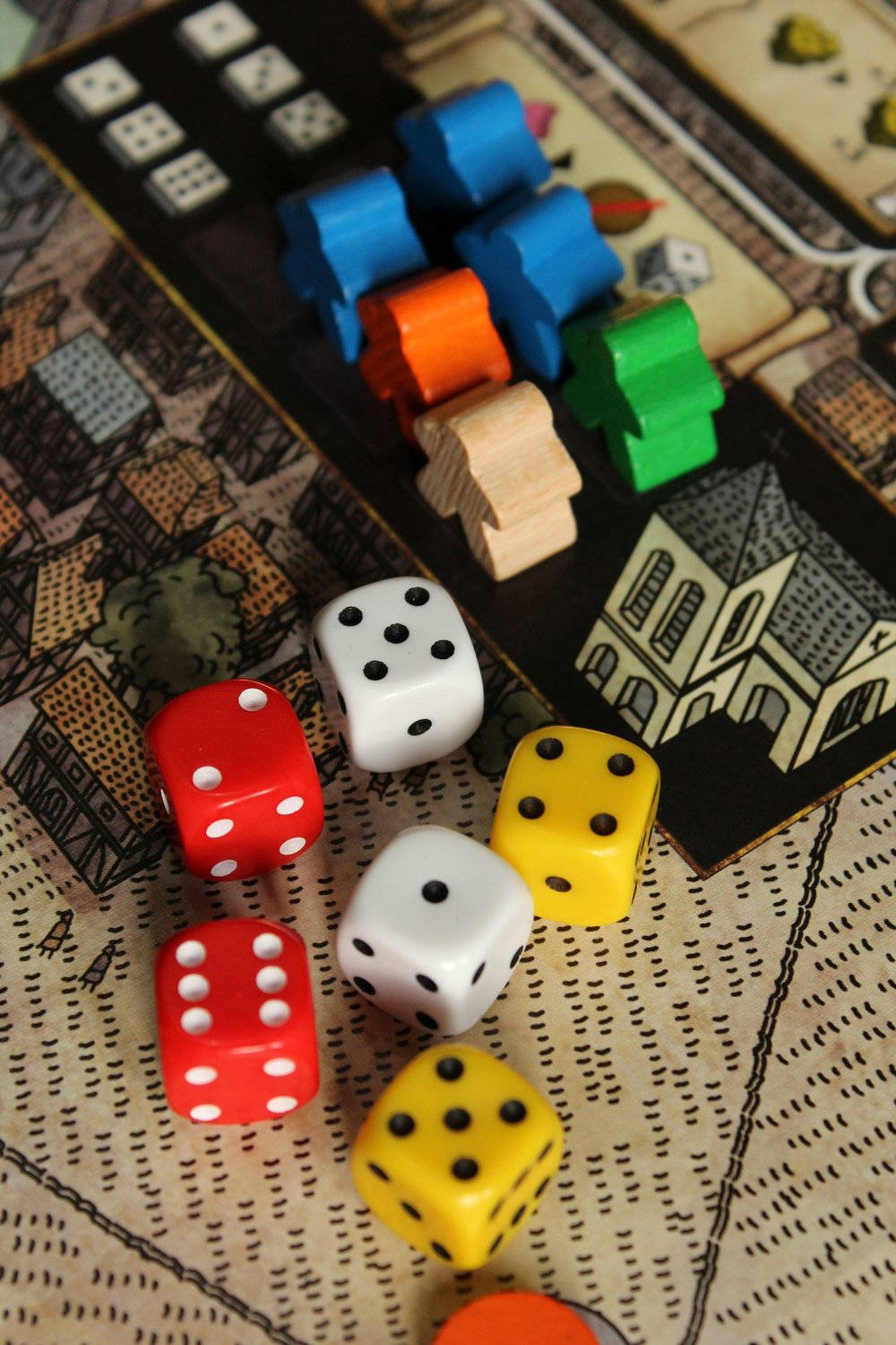桌布 壁紙 — 色彩繽紛的骰子和木製遊戲棋子特寫，位於細節豐富的棋盤遊戲地圖上，地圖上有插圖建築物。
