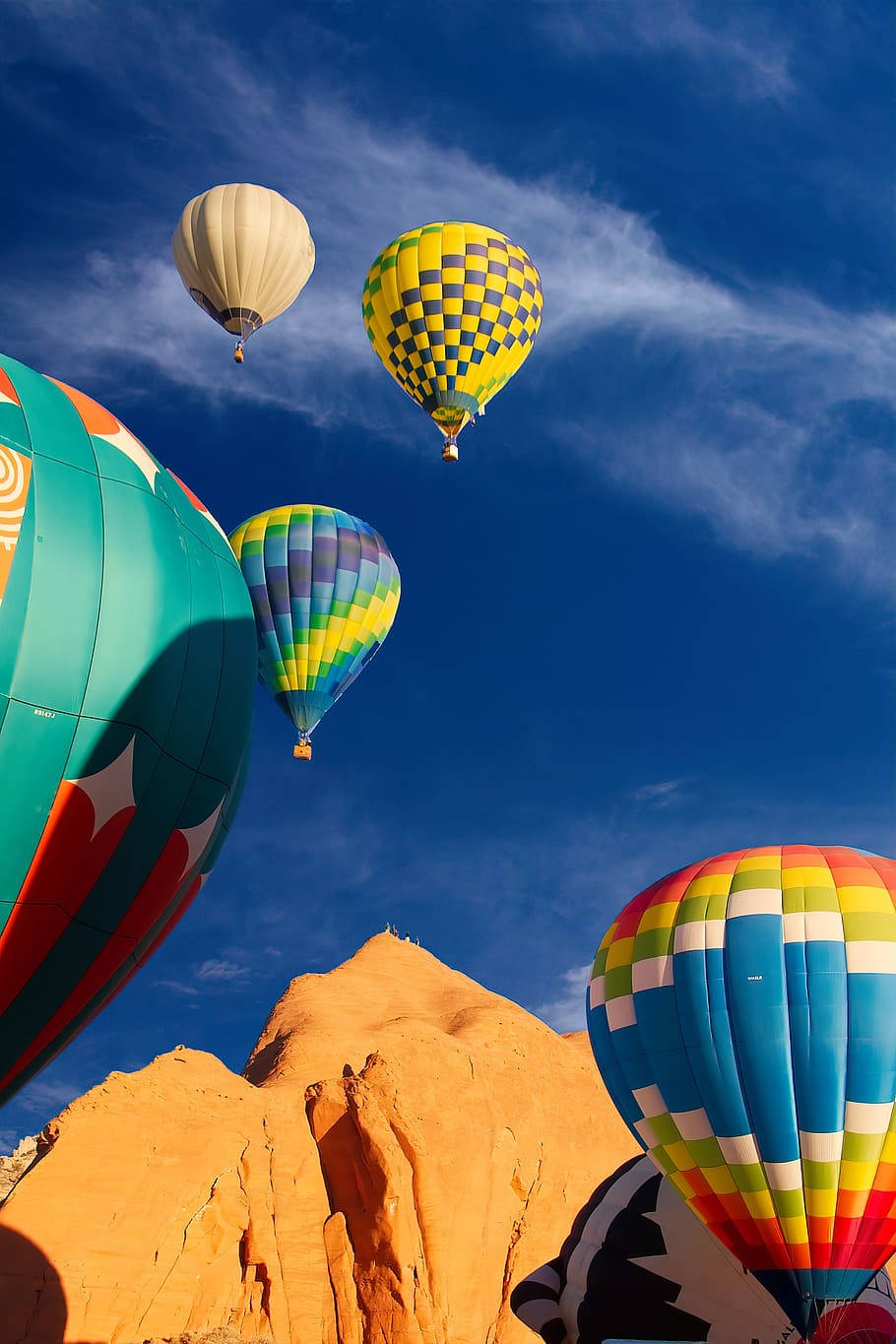Hot Air Balloon 桌布 壁紙 — 色彩鮮豔、圖案大膽的熱氣球在深藍色天空襯托下，翱翔於橙色沙漠岩層之上。