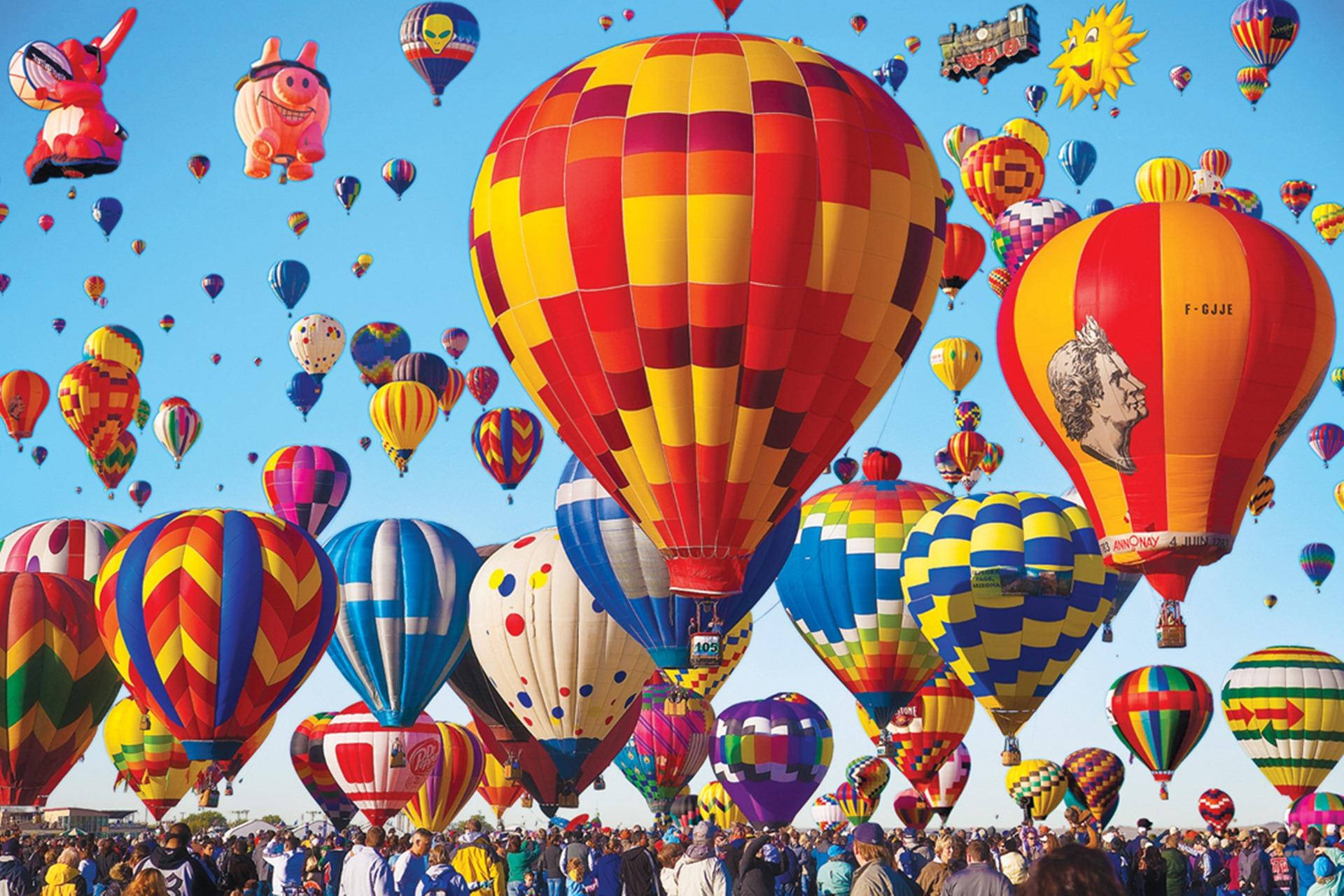 Balloon 桌布 壁紙 — 色彩鮮豔、圖案大膽的熱氣球在節日晴朗的藍天下，飄浮在歡呼的人群上方。
