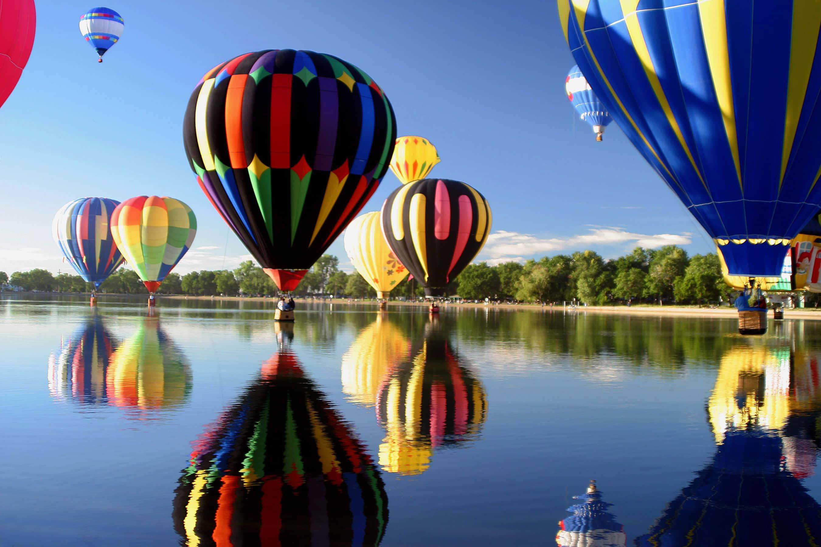 Hot Air Balloon 桌布 壁紙 — 色彩鮮豔、帶有粗條紋的熱氣球漂浮在平靜的湖面上，在清澈的藍天下映照出它們多彩的倒影。