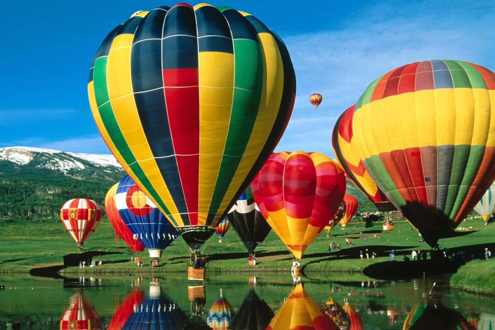 Balloon 桌布 壁紙 — 色彩鮮豔、條紋大膽的熱氣球，在清澈藍天下，完美倒映在平靜的水面上，背景是白雪覆蓋的山峰。