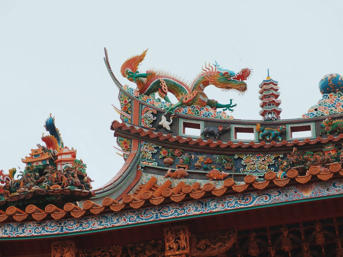 唐人街 桌布 壁紙 — 色彩鮮豔、裝飾華麗的龍雕塑，在淡色天空的襯托下，矗立在傳統瓦片屋頂之上。