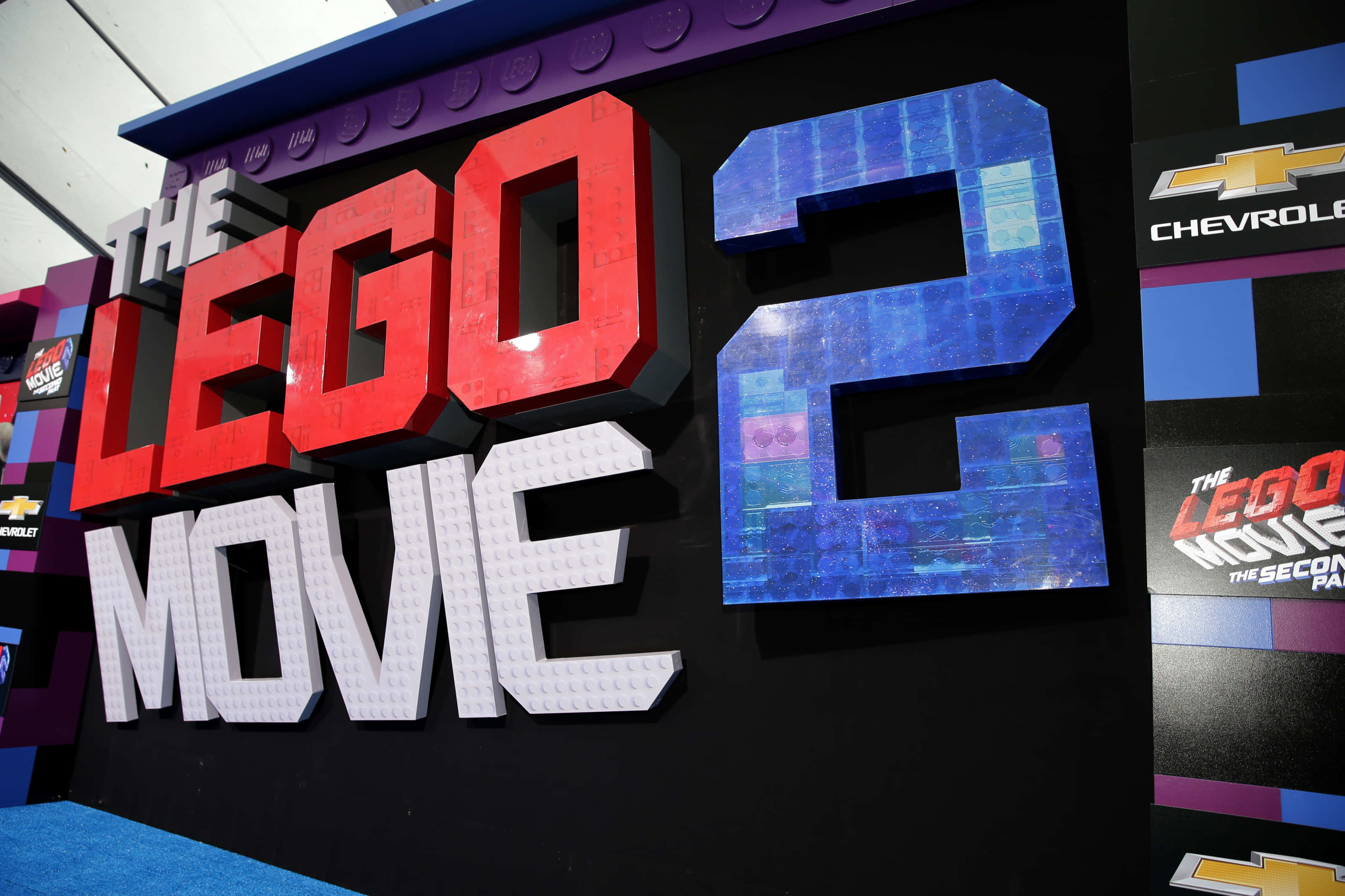 樂高 桌布 壁紙 — 色彩鮮豔的 3D LEGO 電影 2 標題標誌，以紅、白、藍色塊狀字母呈現，背景為黑色。