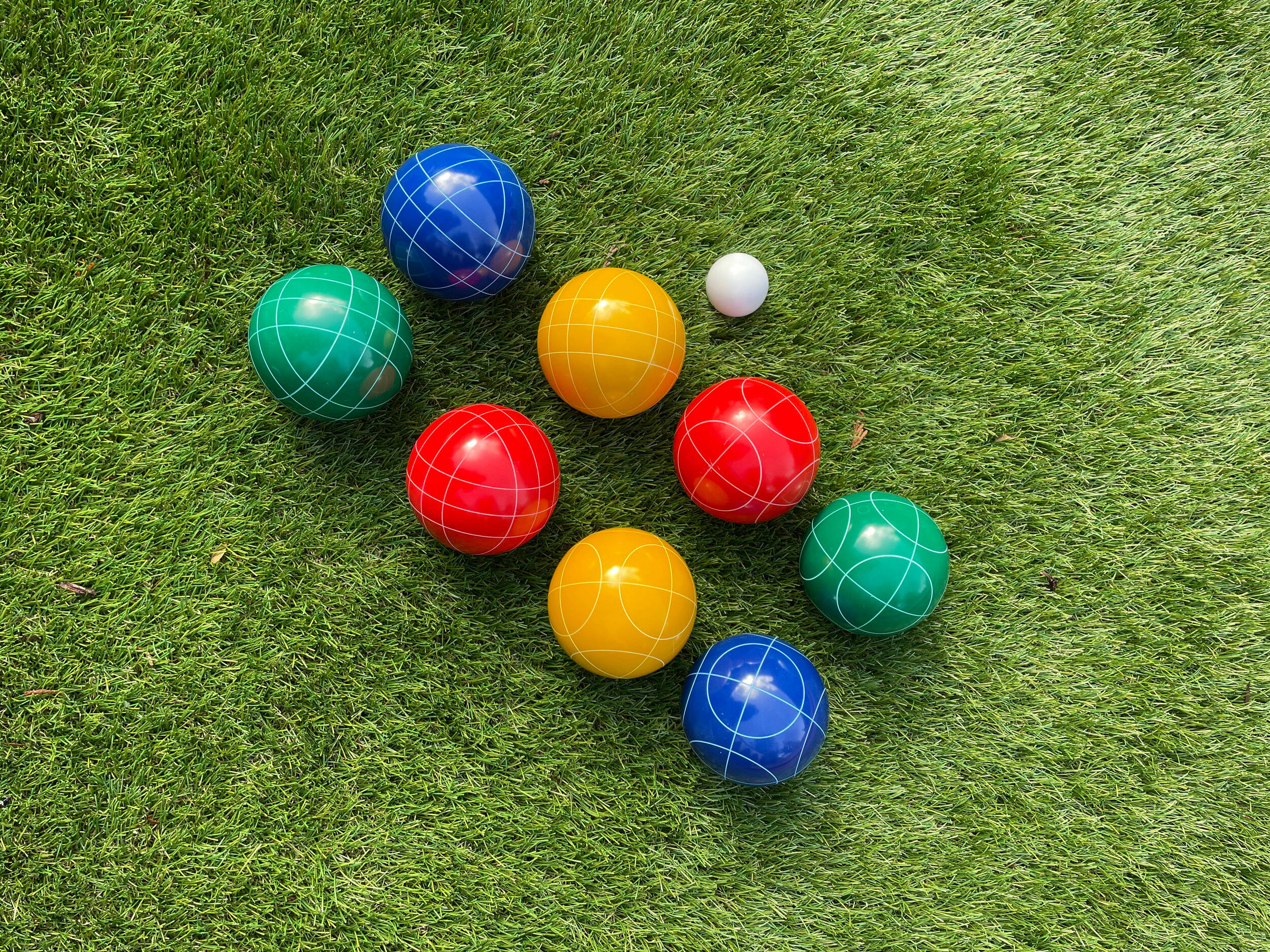 運動 桌布 壁紙 — 色彩鮮豔的滾球（Bocce）帶有白色網格線，在明亮的日光下放置在茂密的綠草地上。
