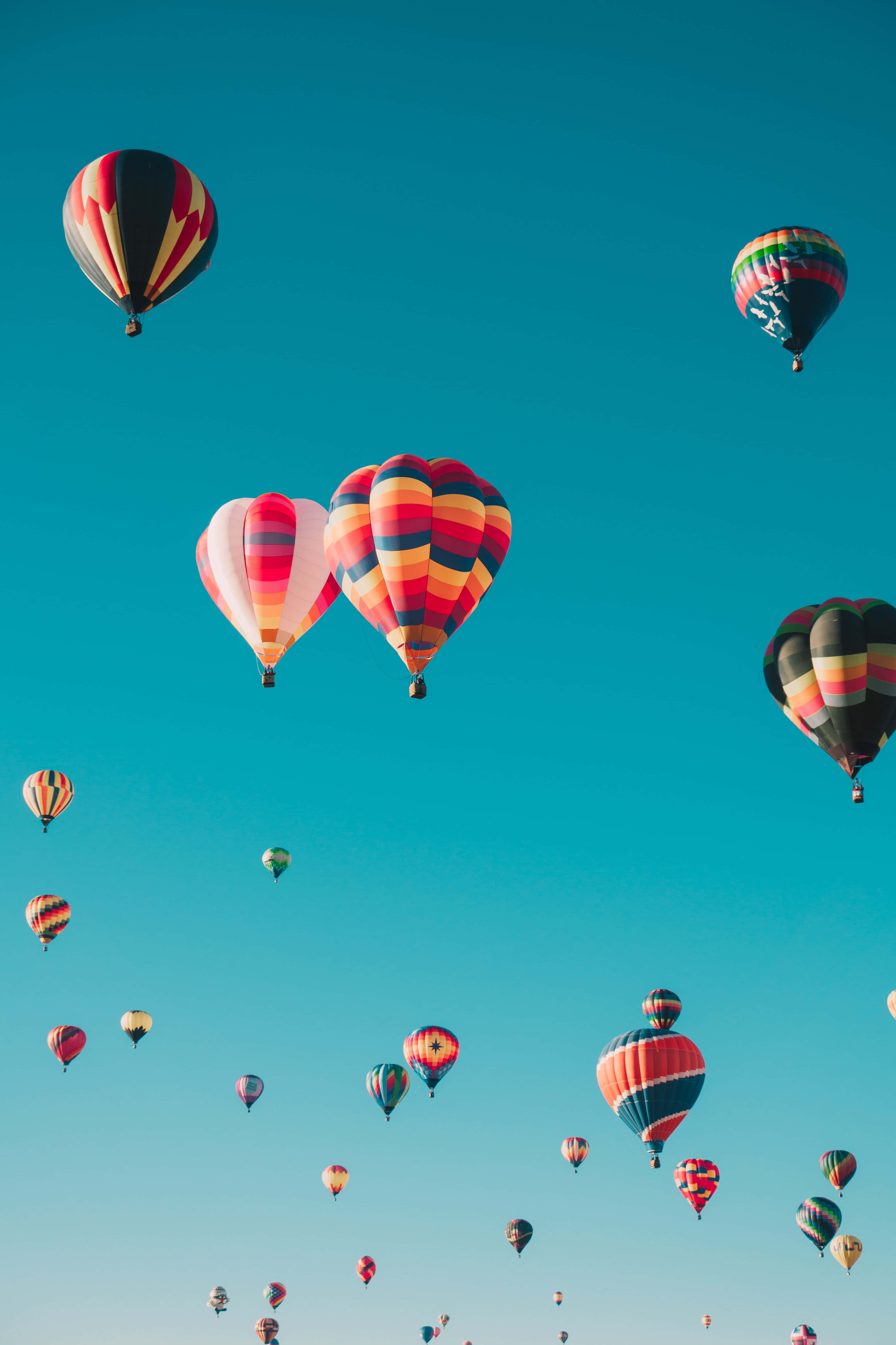 Balloons 桌布 壁紙 — 色彩鮮豔的熱氣球帶有醒目圖案，在清澈的藍綠色天空中飄移，形成節日般的空中聚會。