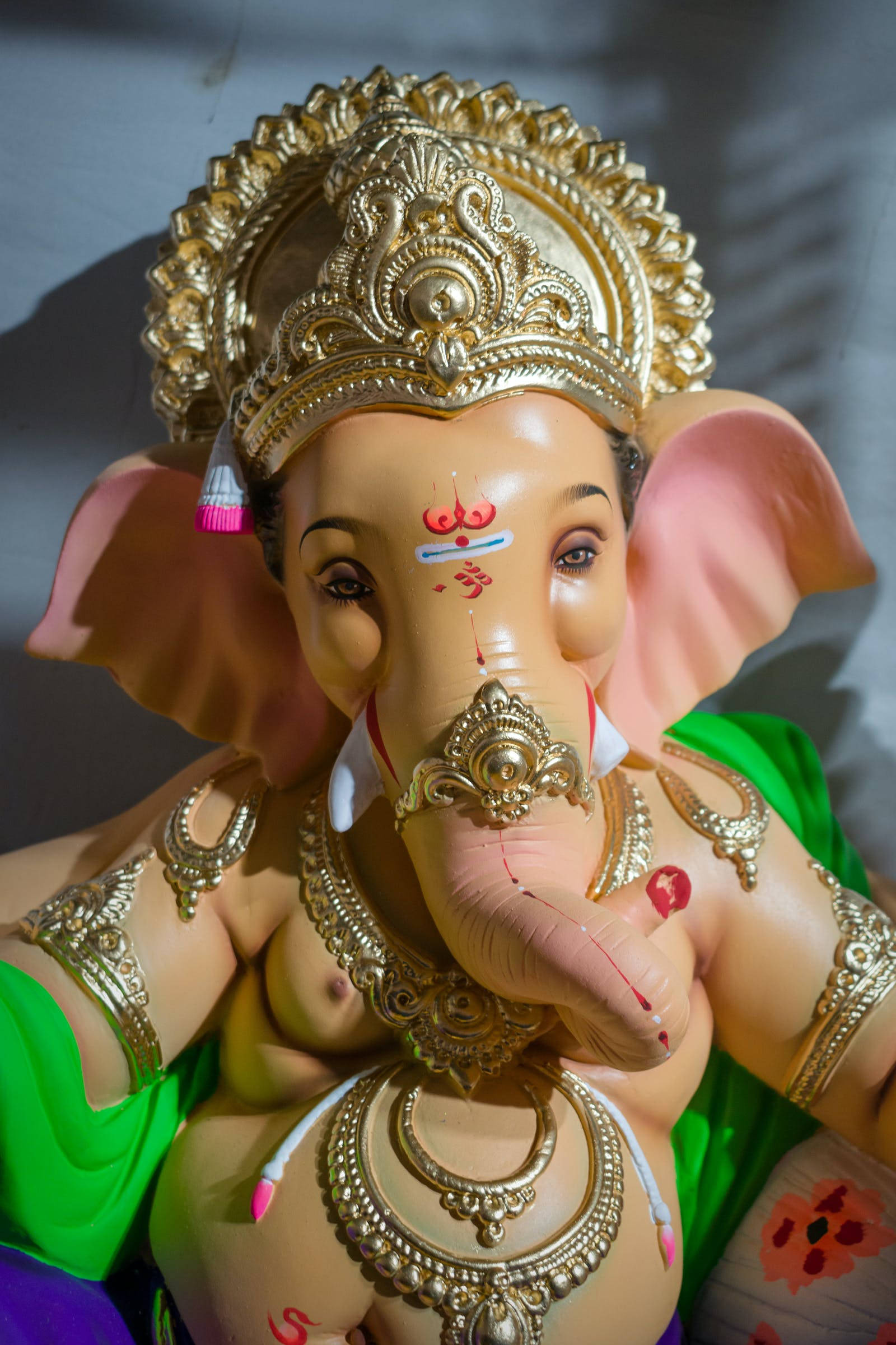 Vinayaka 桌布 壁紙 — 色彩鮮豔的象神雕像特寫，飾有黃金珠寶和綠色布料，在明亮的陽光下。
