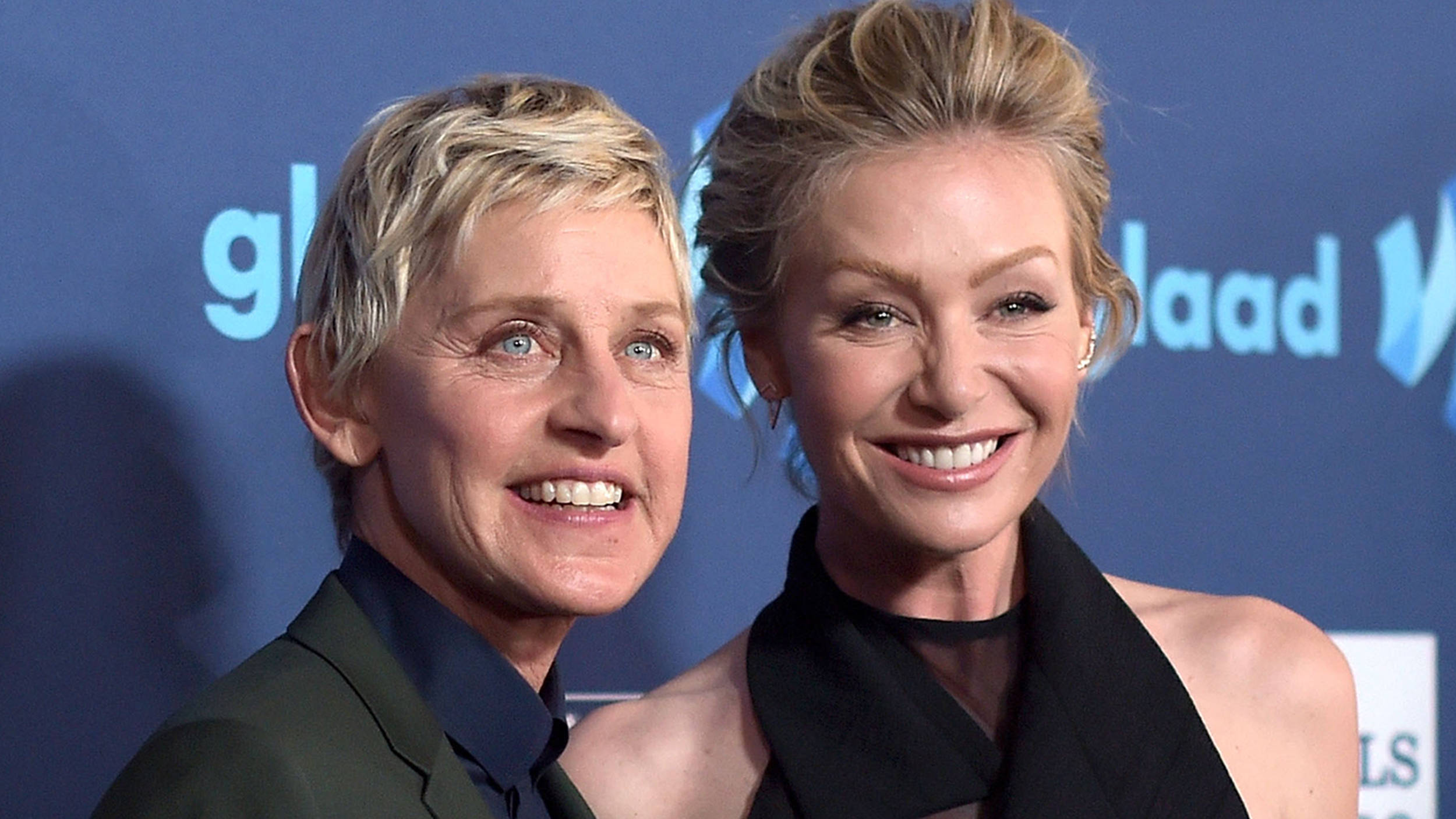 Ellen Degeneres 桌布 壁紙 — 艾倫·狄珍妮絲和波蒂亞·德羅西在GLAAD活動中，在藍色品牌背景前燦爛微笑。