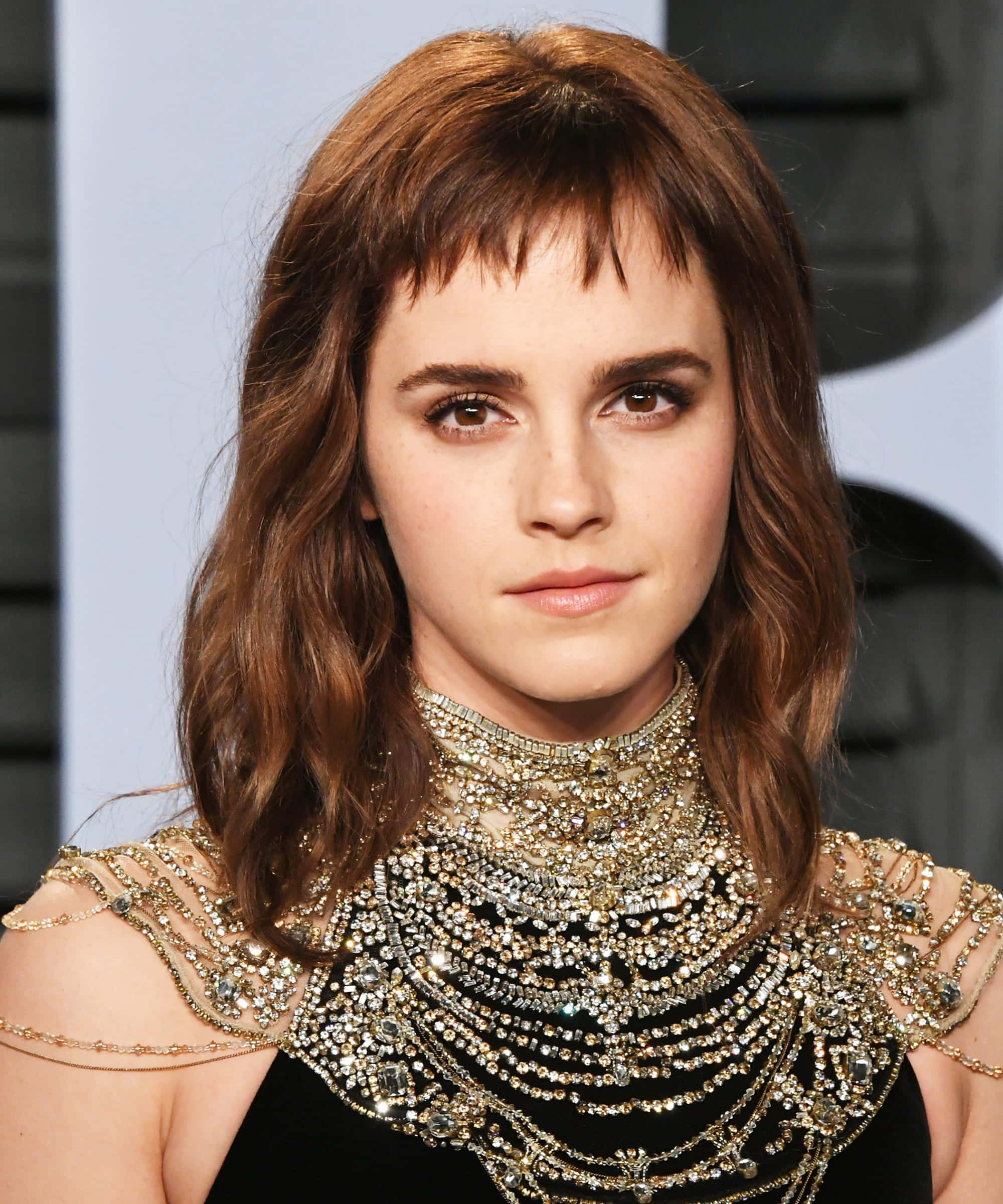 Emma Watson 桌布 壁紙 — 艾瑪華森以沉穩表情直視前方，身穿飾有精緻肩部細節的華麗黑金鑲寶石長裙。