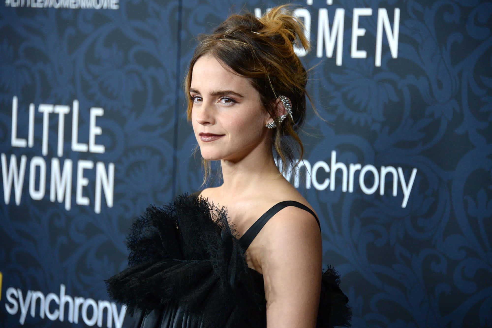 Emma Watson 桌布 壁紙 — 艾瑪華森在《她們》首映會上，身穿黑色羽毛禮服，在深藍色圖案背景前優雅地擺姿勢。