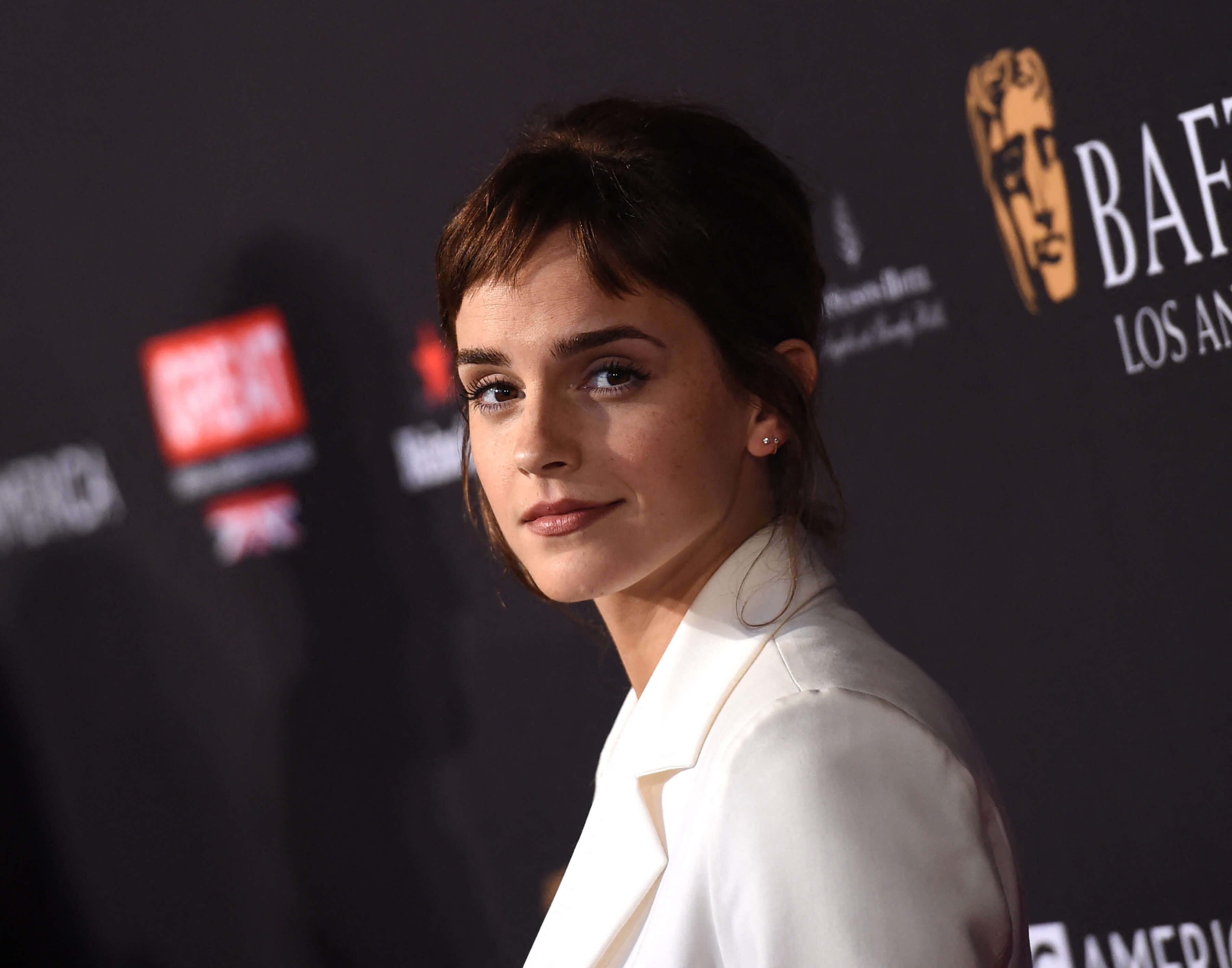 Emma Watson 桌布 壁紙 — 艾瑪華森在BAFTA活動中穿著白色西裝外套，在深色品牌背景前擺姿勢。