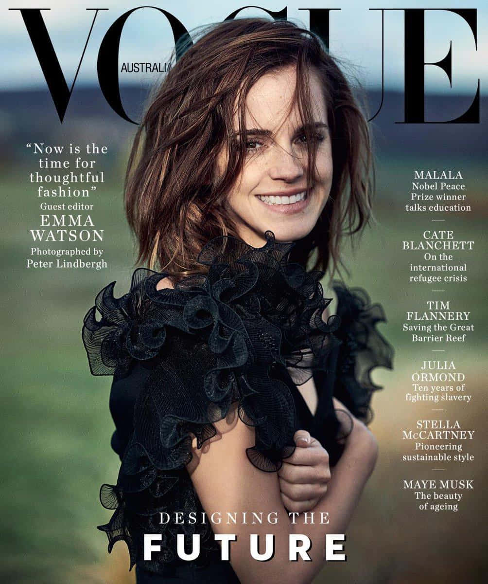 Emma Watson 桌布 壁紙 — 艾瑪華森在Vogue Australia封面上，穿著黑色荷葉邊連衣裙，在模糊的綠色田野背景下燦爛微笑。