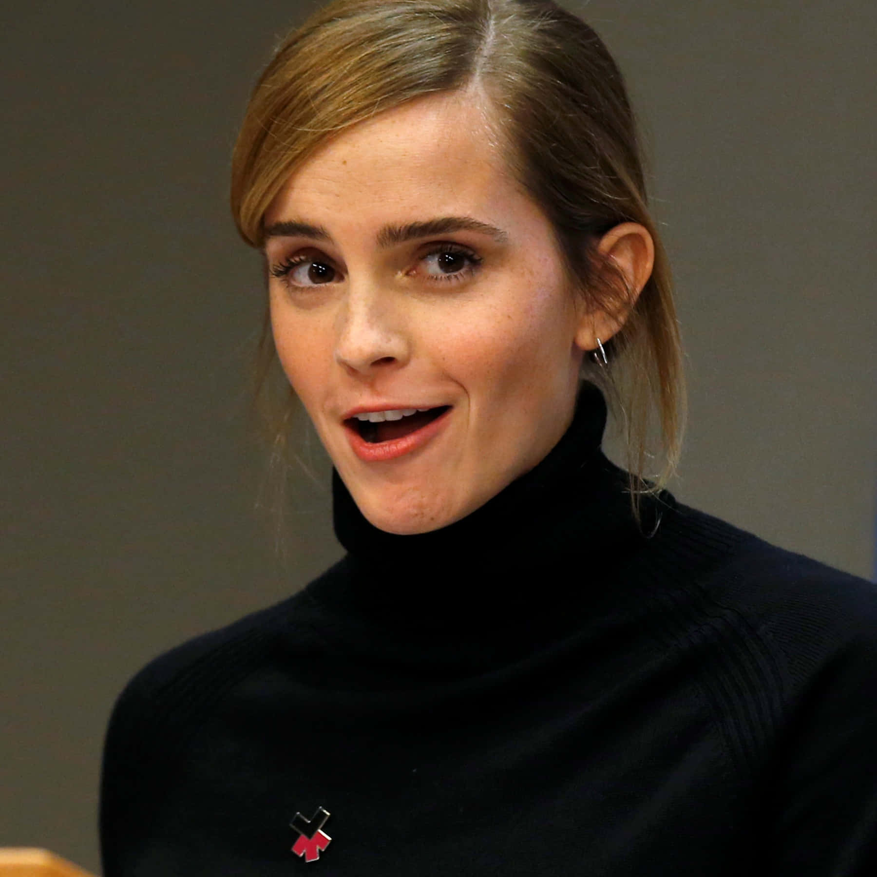 Emma Watson 桌布 壁紙 — 艾瑪華森穿著黑色高領毛衣，在純灰色背景前溫暖地微笑。