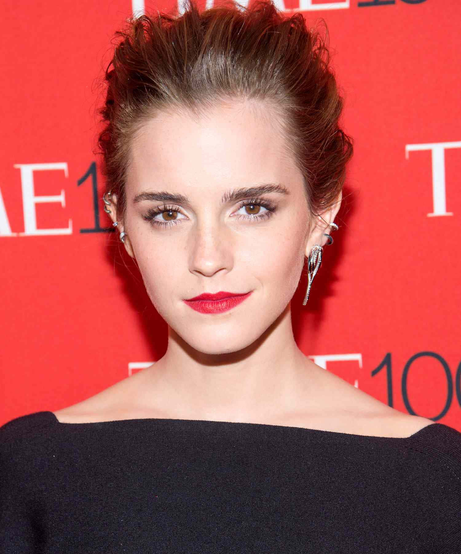 Emma Watson 桌布 壁紙 — 艾瑪華森自信地擺姿勢，身穿黑色露肩上衣，背景是鮮紅色的活動背景板，上面有白色文字。
