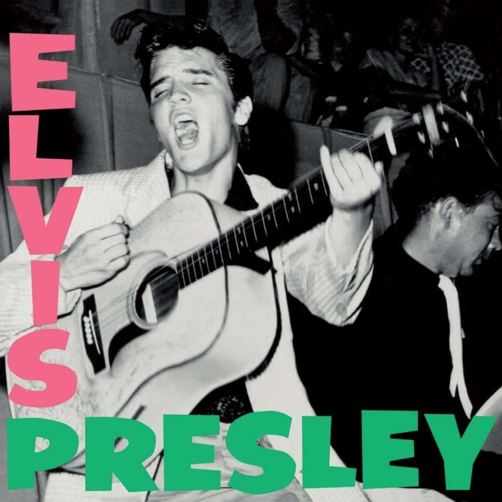Elvis 桌布 壁紙 — 艾維斯·普里斯萊在黑白照片中熱情演唱並彈奏原聲吉他，上面覆蓋著大膽的粉紅色和綠色文字。