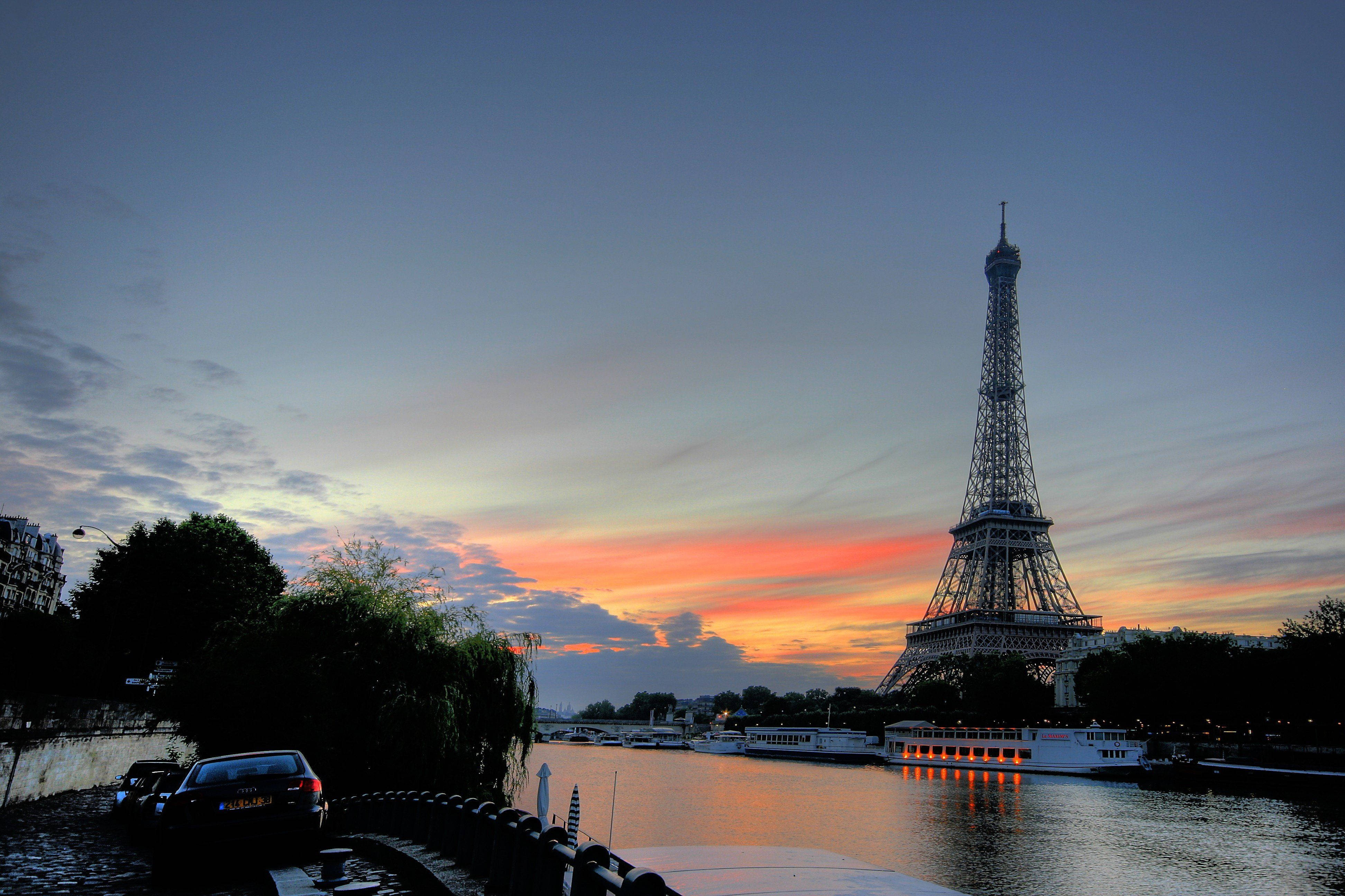 Paris Eiffel Tower 桌布 壁紙 — 艾菲爾鐵塔在充滿活力的日落天空下呈現剪影，橙色和粉紅色的雲彩倒映在塞納河中。