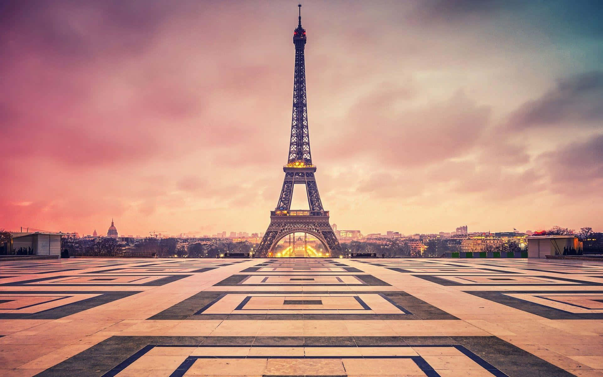 Eiffel Tower 桌布 壁紙 — 艾菲爾鐵塔在充滿活力的粉紅色和橙色日落天空下高高聳立，為下方幾何圖案廣場投下溫暖的光芒。